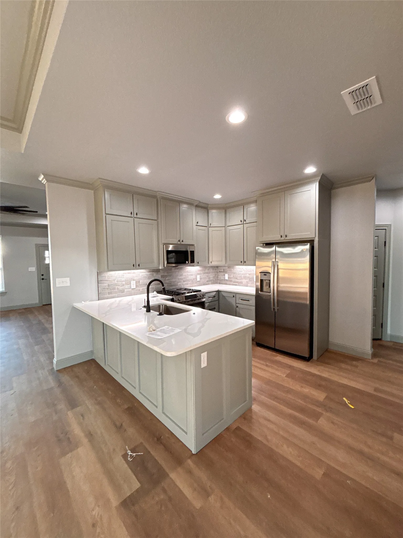 Contemporary kitchen featuring light gray cabinetry, stainless steel appliances, white countertops, and a white subway tile backsplash