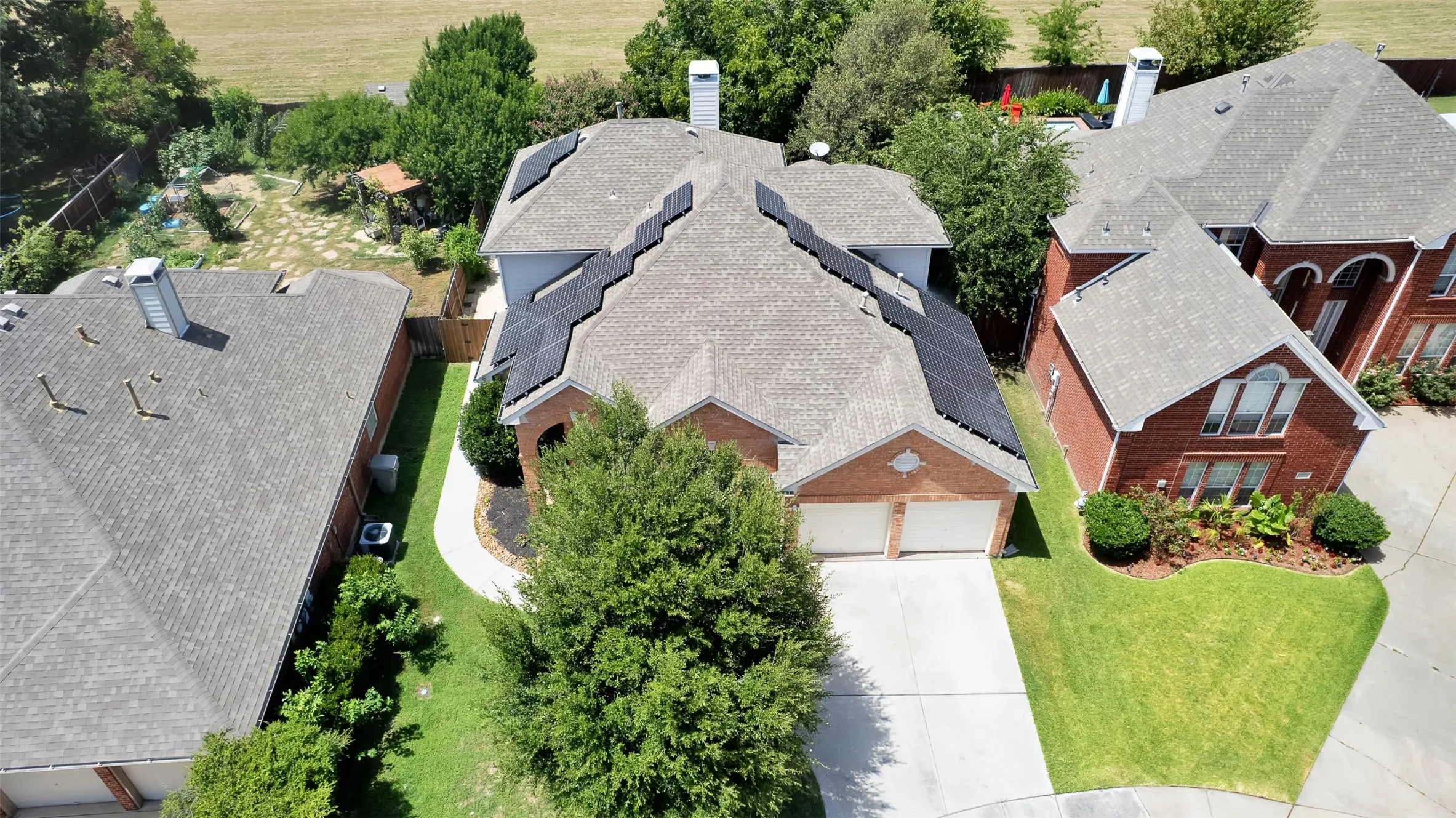 Brick exterior residence featuring a two-car garage, solar panel installation, a gray shingle roof, and a paved driveway