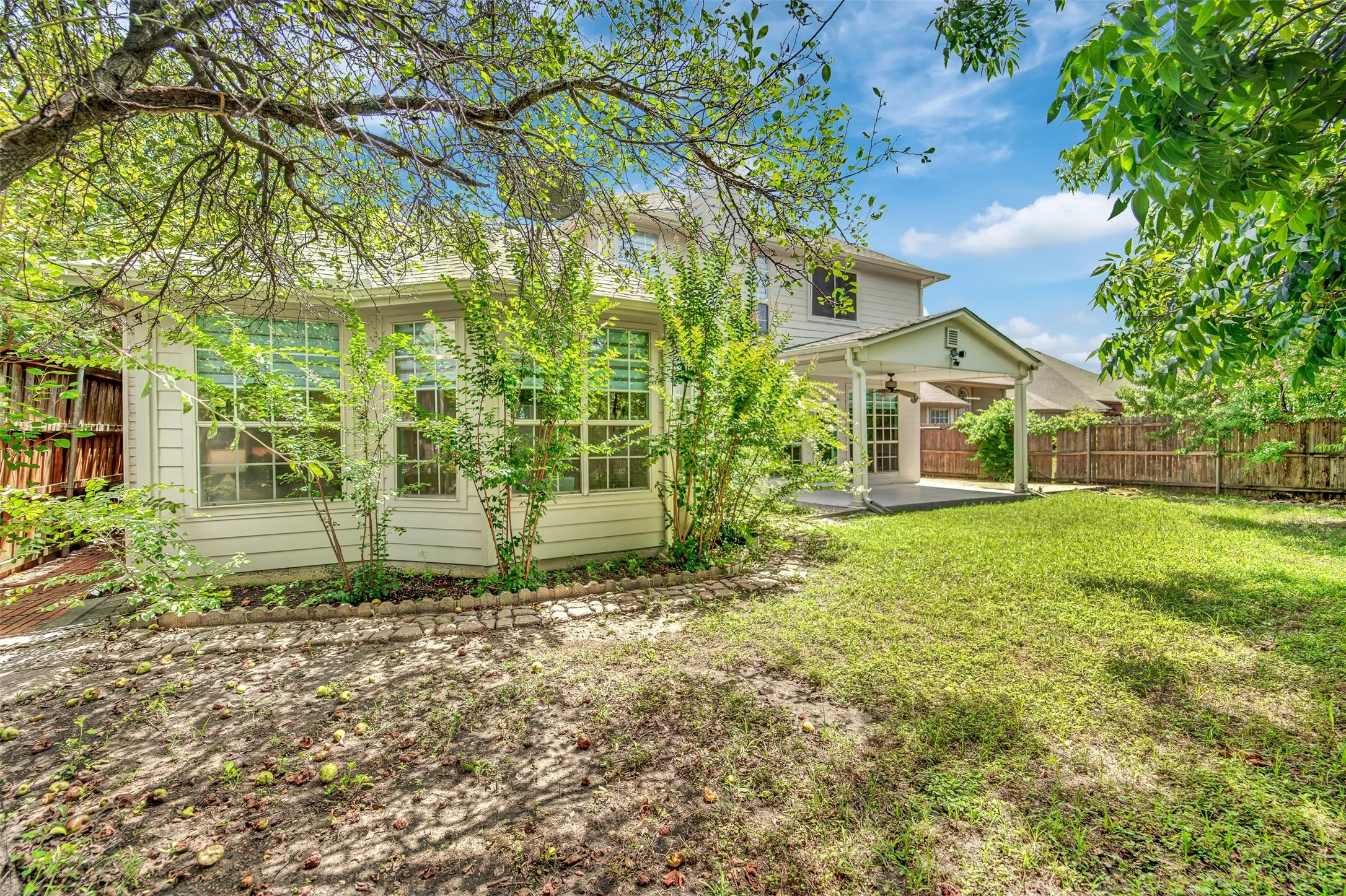 Expansive backyard featuring a covered patio with a ceiling fan, a manicured lawn, and mature trees providing natural shade