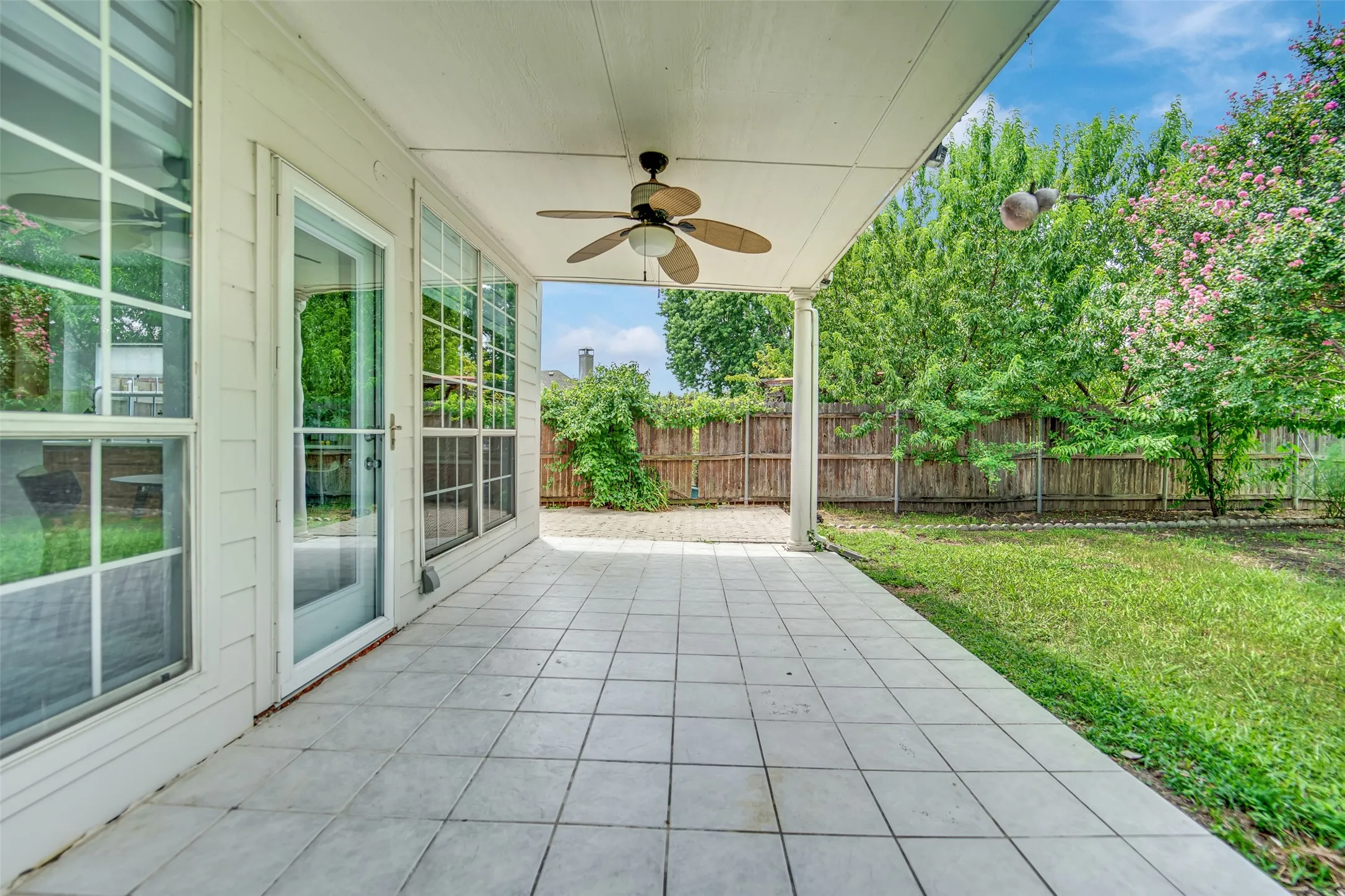 Covered patio with square tile flooring extending to a fenced backyard with mature trees
