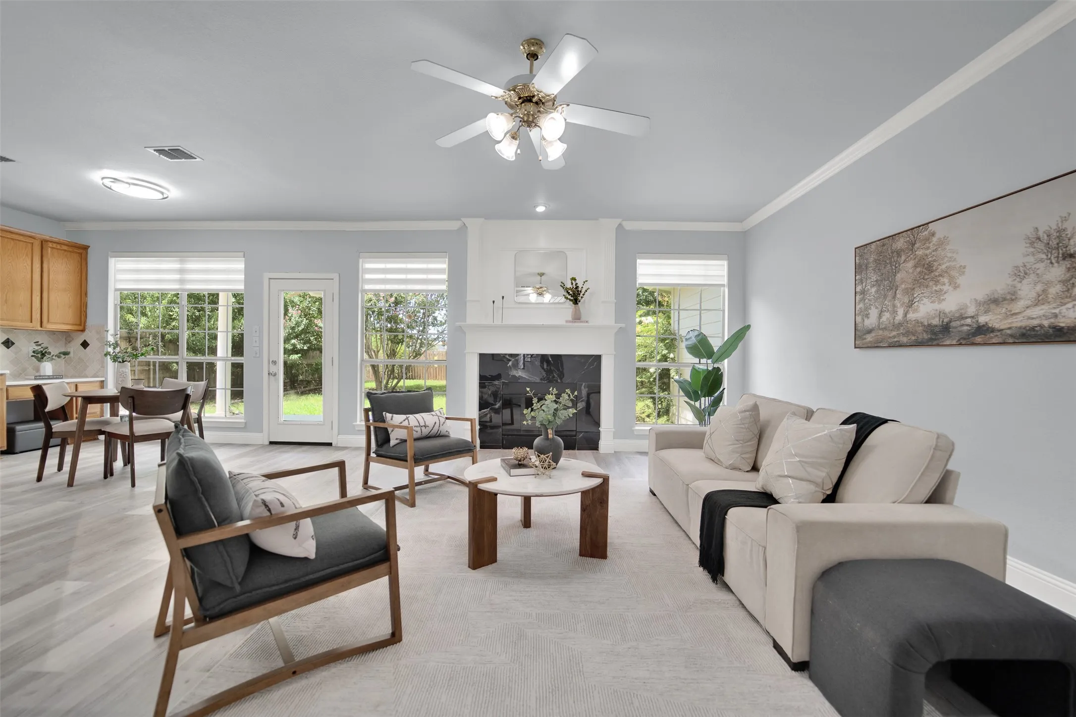 Living area featuring a fireplace with white mantel, light wood-finish flooring, multiple windows, a glass-paned door, and crown molding