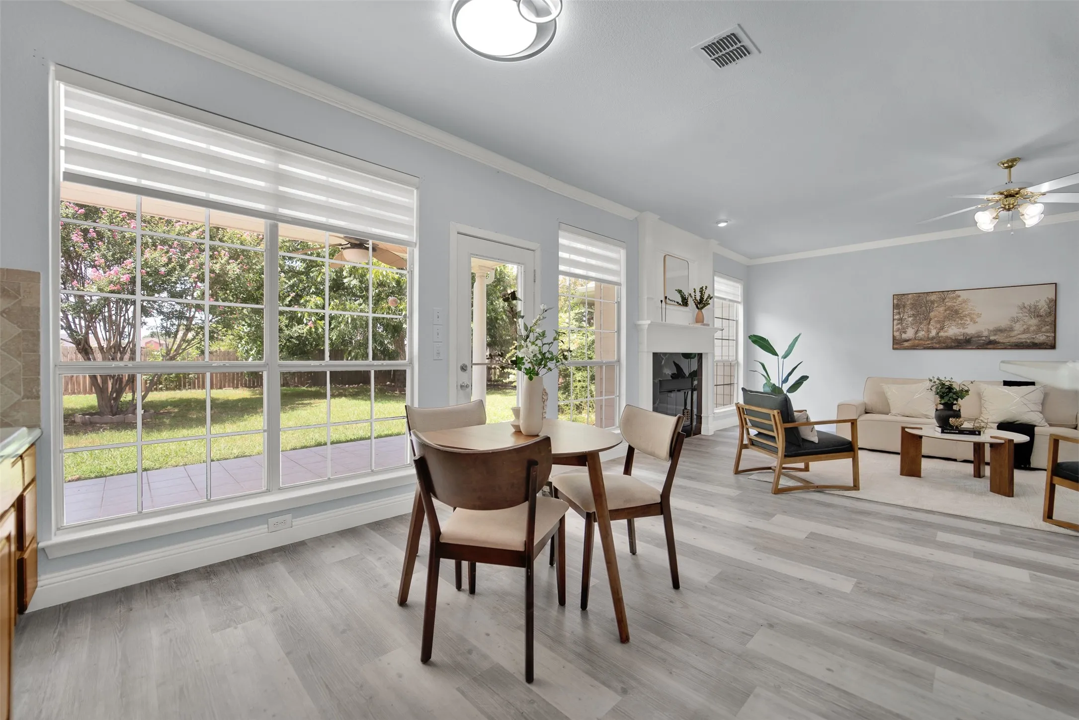 Open-concept living space with light wood-finish flooring, a white mantel fireplace, and crown molding