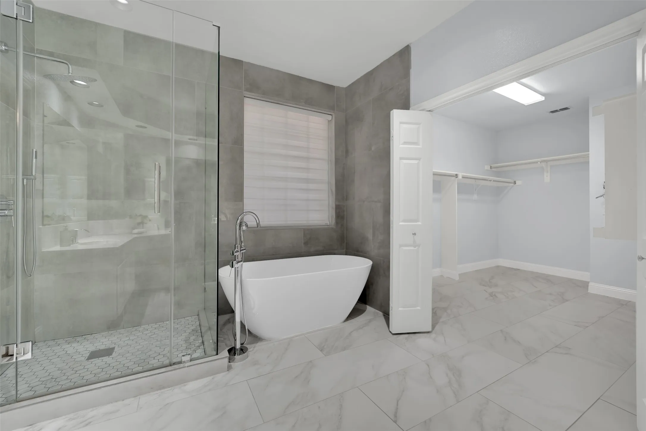 Freestanding soaking tub with a floor-mounted fixture, glass-enclosed shower, and a built-in closet with shelving and hanging rods