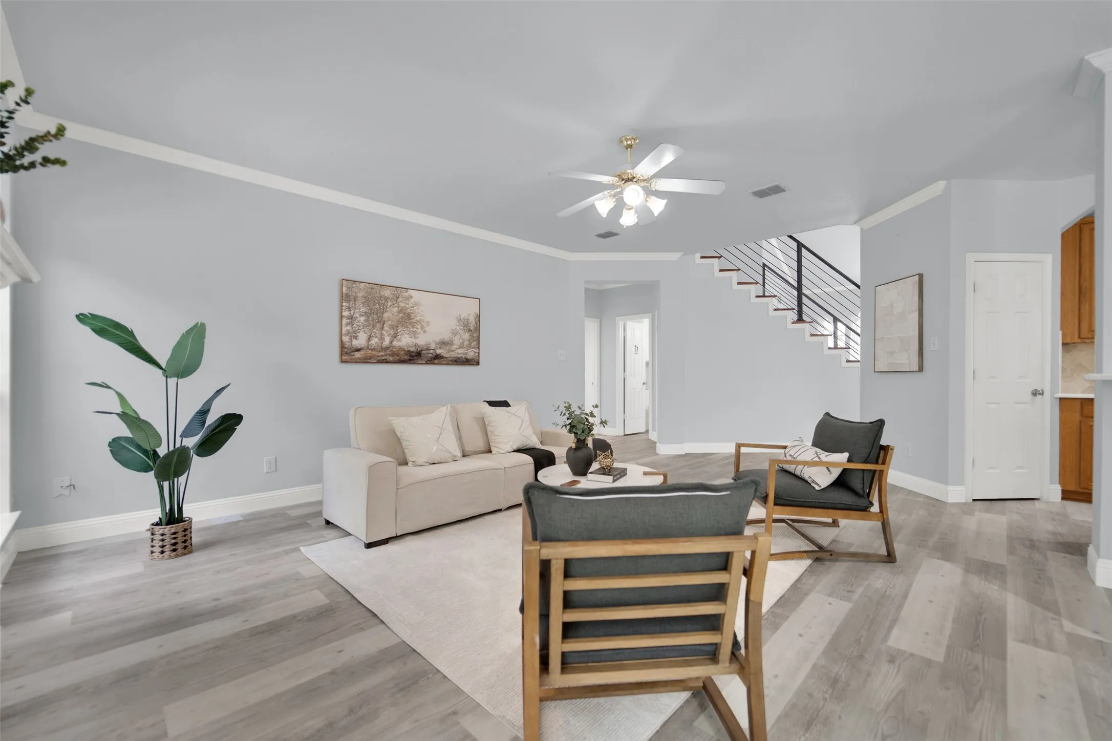 Spacious living area featuring wood-finish flooring, light blue walls, and white crown molding