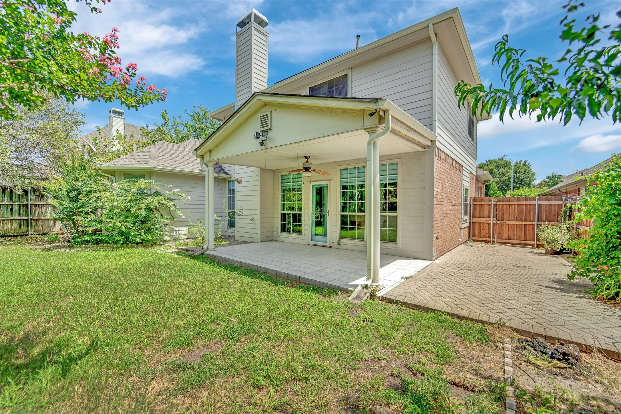 Spacious backyard featuring a covered patio, extensive lawn area, and a brick paver pathway