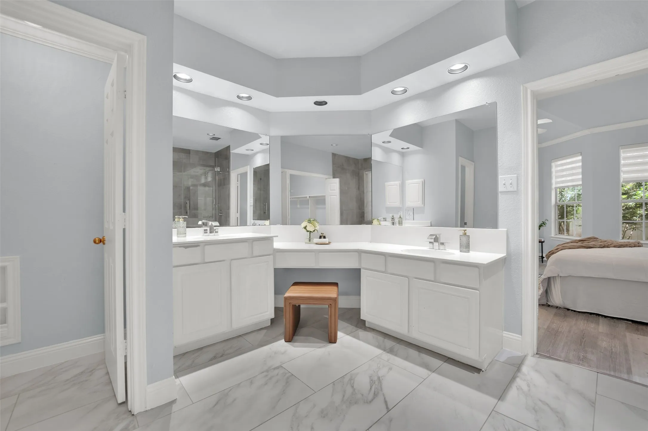 Spacious bathroom featuring a dual vanity with white cabinetry and integrated sinks, a built-in makeup vanity, large mirrors, recessed lighting, and marble-look tile flooring