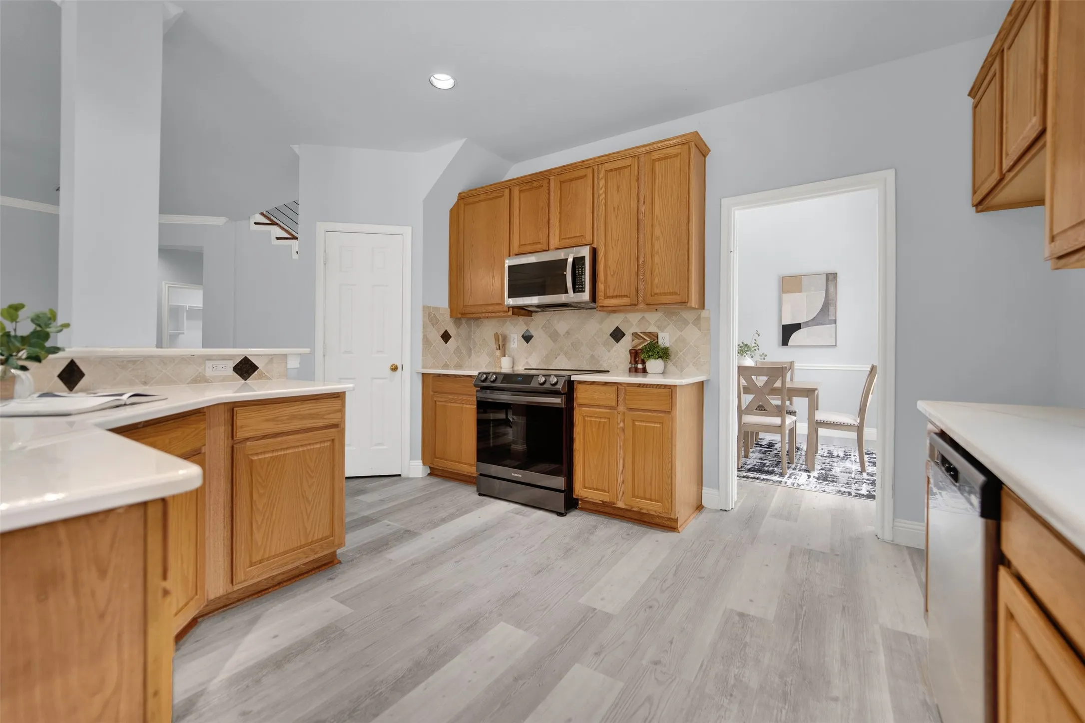 Kitchen featuring light wood cabinetry, light countertops, stainless steel microwave, black range, and wood-finish flooring