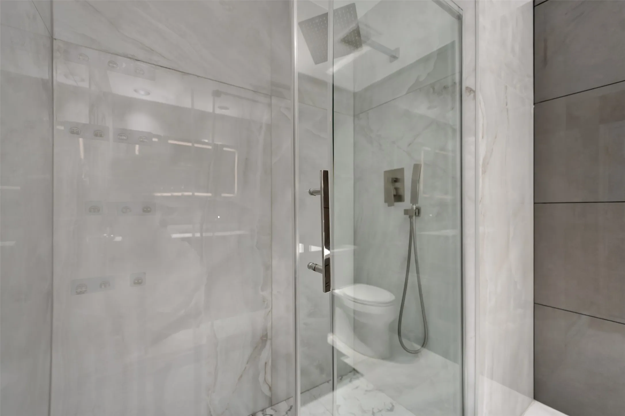 Modern bathroom featuring a glass-enclosed shower with a rainfall showerhead, handheld spray, and integrated body jets