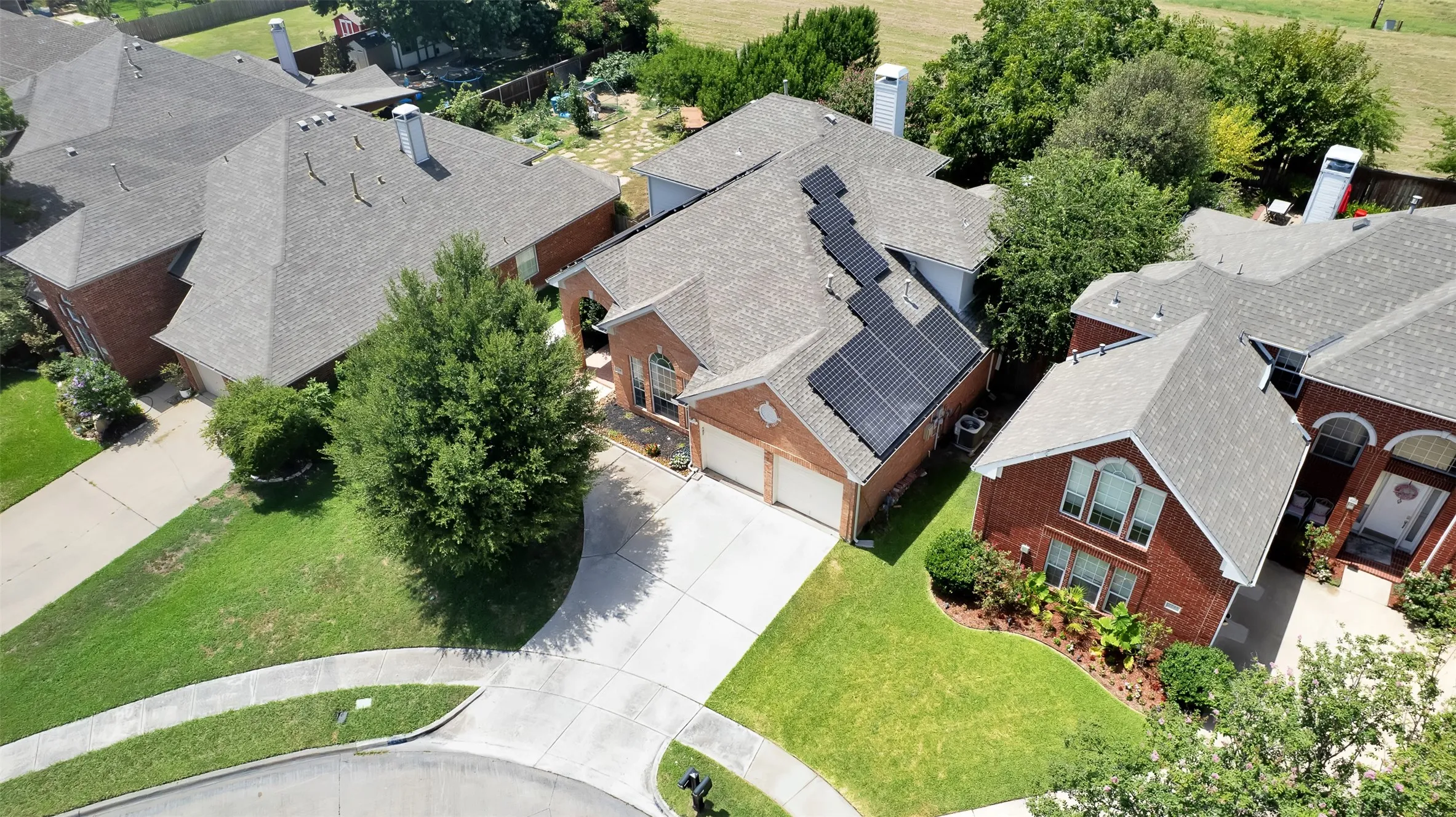Brick exterior residence featuring a two-car garage, mature front yard landscaping, and solar panel installation