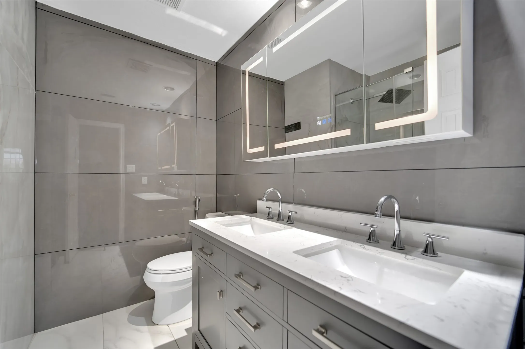 Dual vanity with integrated sinks and chrome fixtures, set against a backdrop of panelized gray walls
