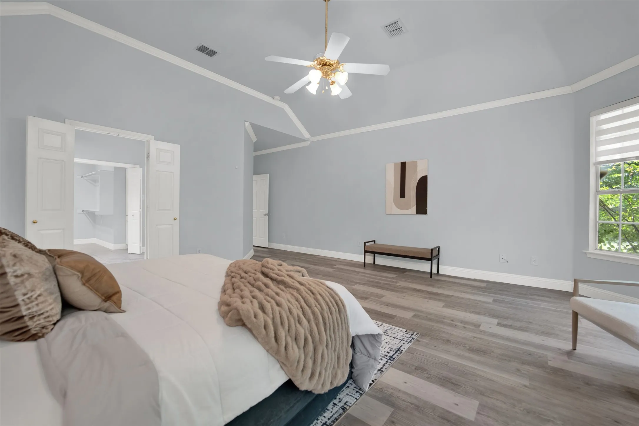 Vaulted ceiling bedroom with light wood-finish flooring, crown molding, and a ceiling fan