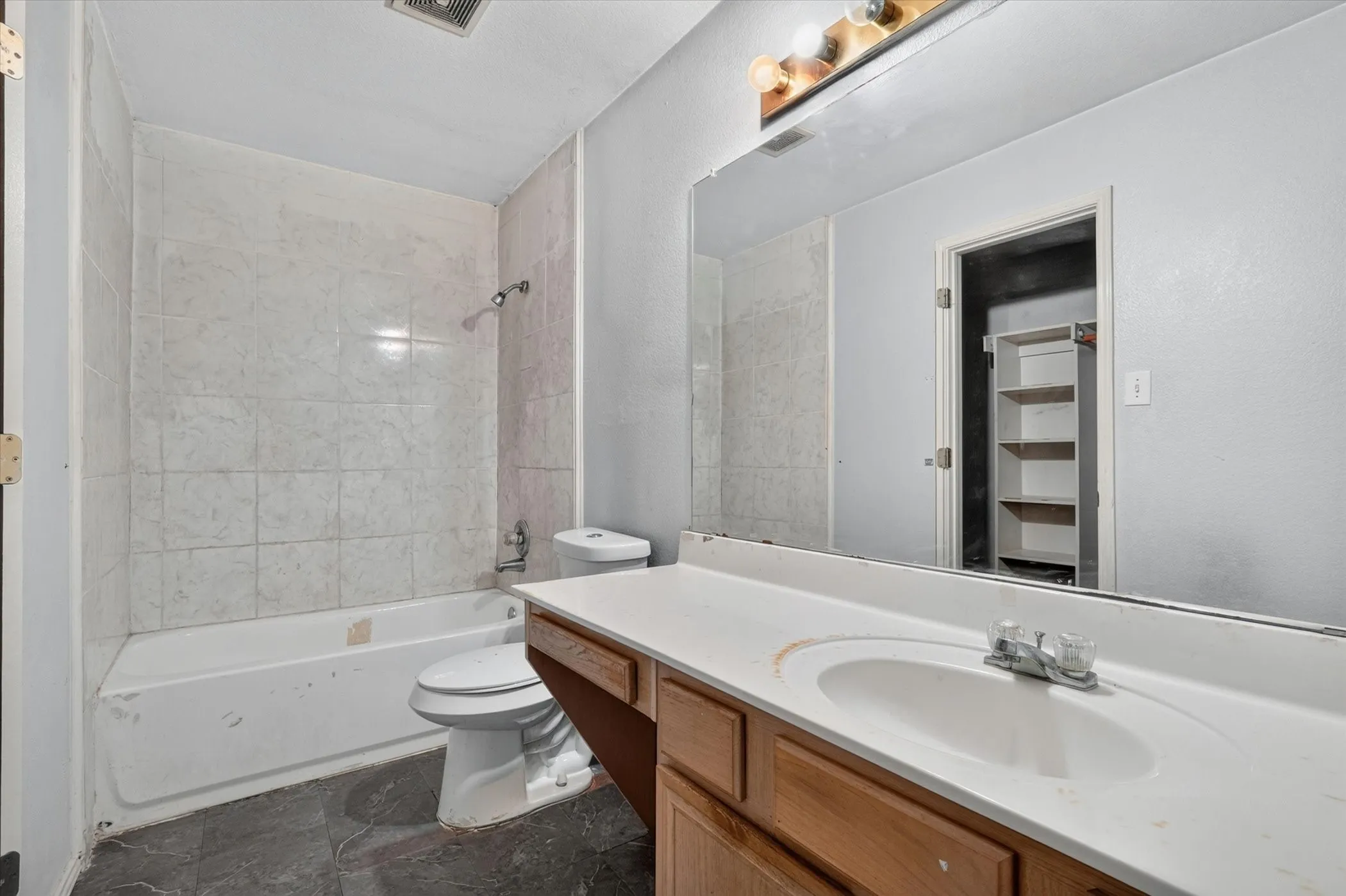Bathroom featuring a full vanity with a built-in sink and wood-finish cabinetry, a large wall-mounted mirror, and a tub-shower combination with tiled walls