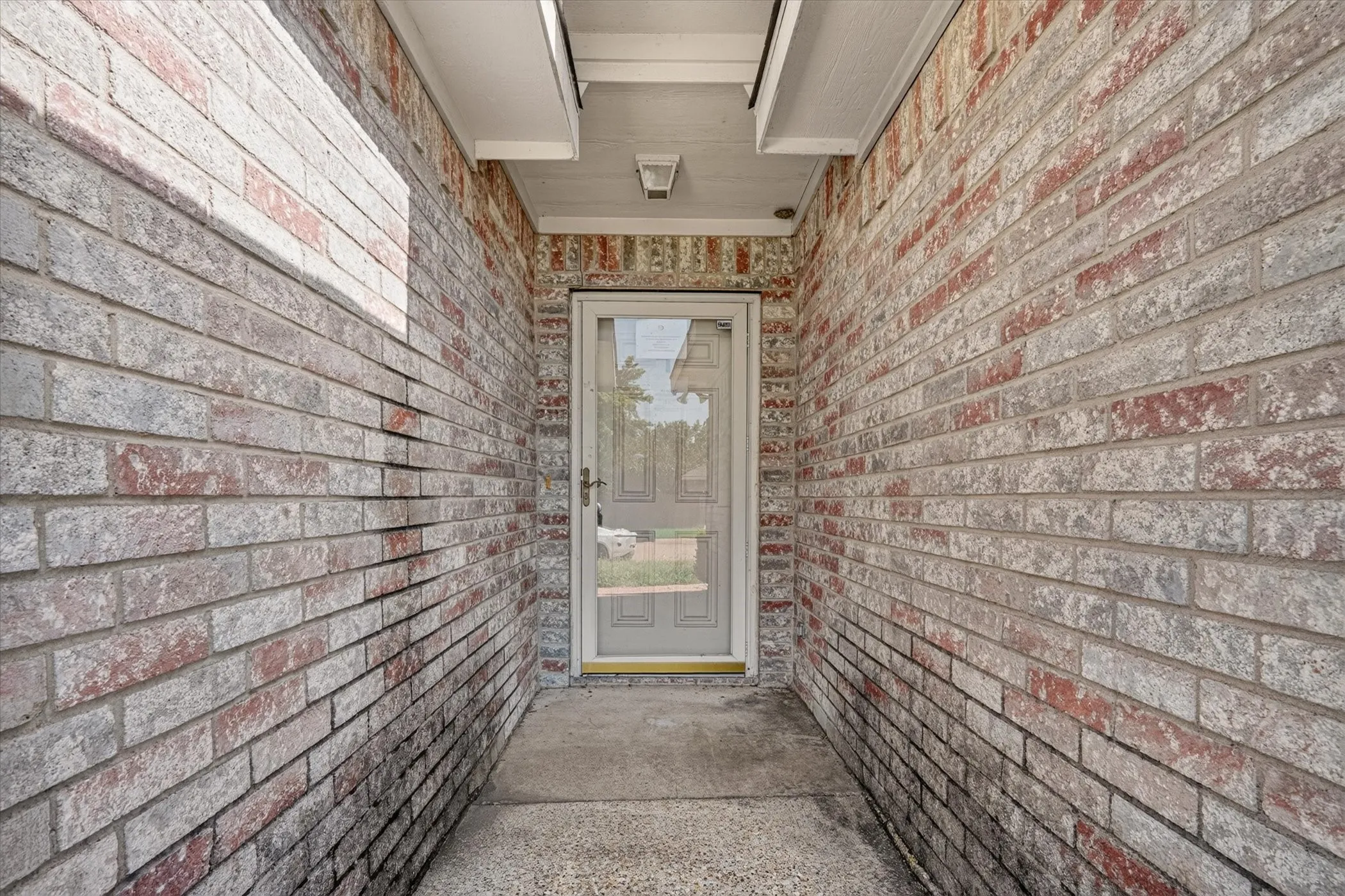 Entryway featuring mixed-tone brick siding and a storm door