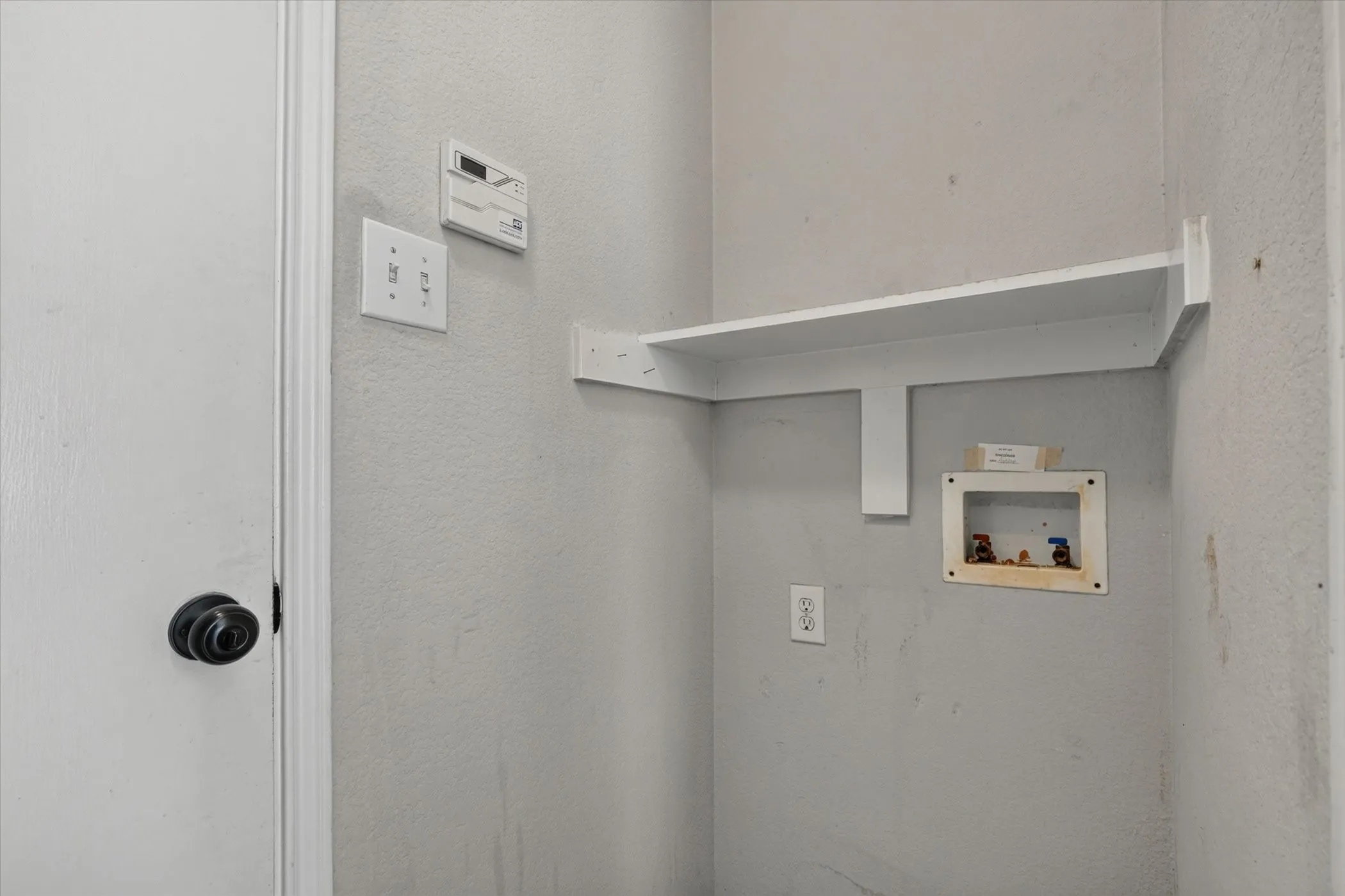 Dedicated laundry space featuring a built-in white shelf, utility hookups, and electrical outlet