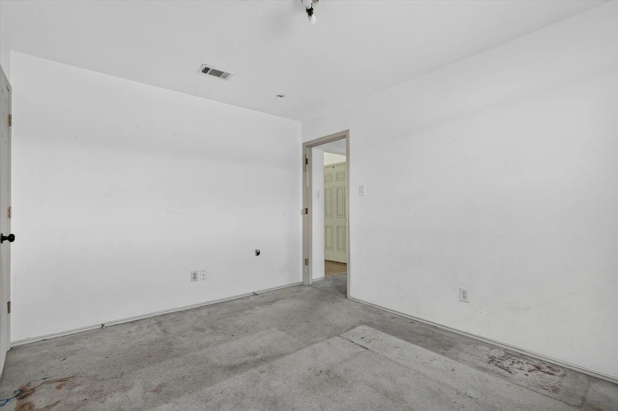White-painted interior walls with a gray carpeted floor, featuring a doorway leading to another interior space