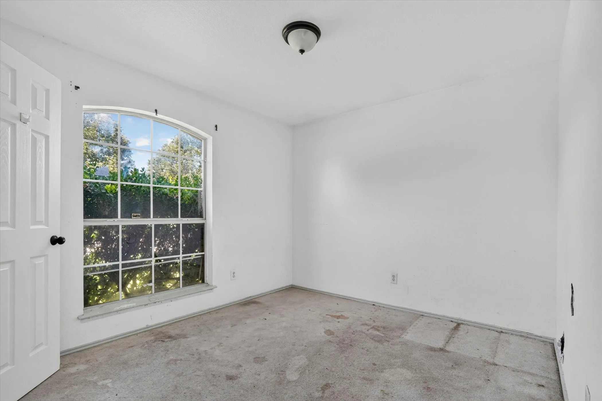 Room featuring a large arched window with multiple panes, white walls, and a ceiling-mounted light fixture