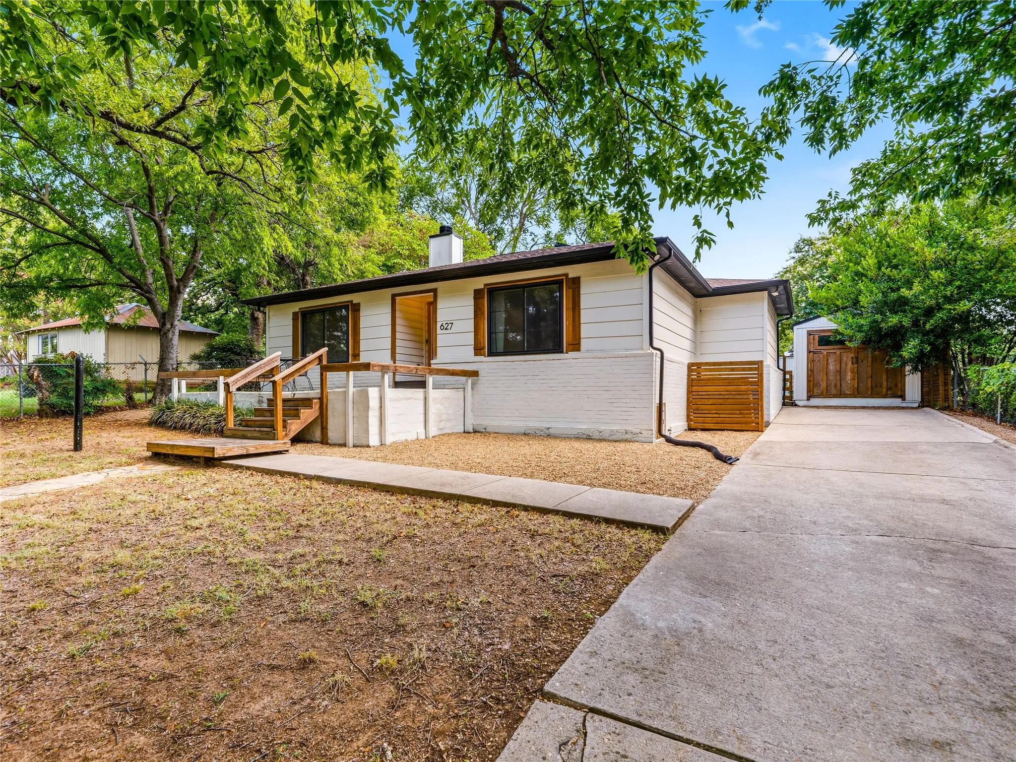 Ranch-style residence featuring white siding and brick, a front porch with natural wood decking and railings, and a concrete driveway