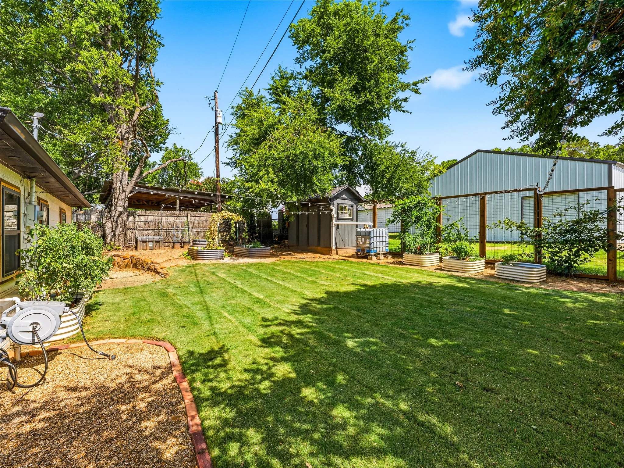 Expansive backyard featuring a lush lawn, raised garden beds, a storage shed, and a privacy fence