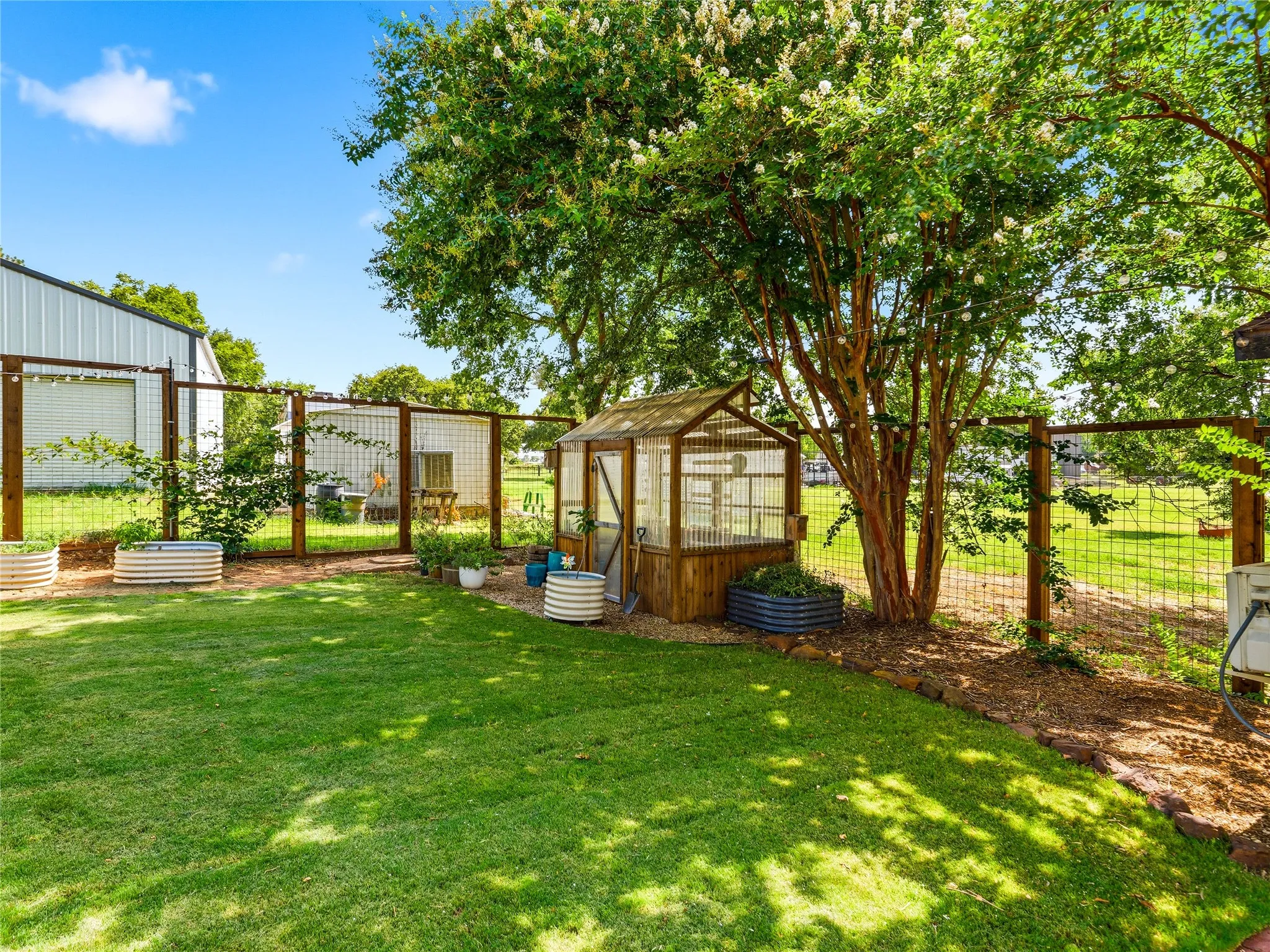 Expansive backyard featuring a lush lawn, a dedicated greenhouse structure, and mature trees providing natural shade