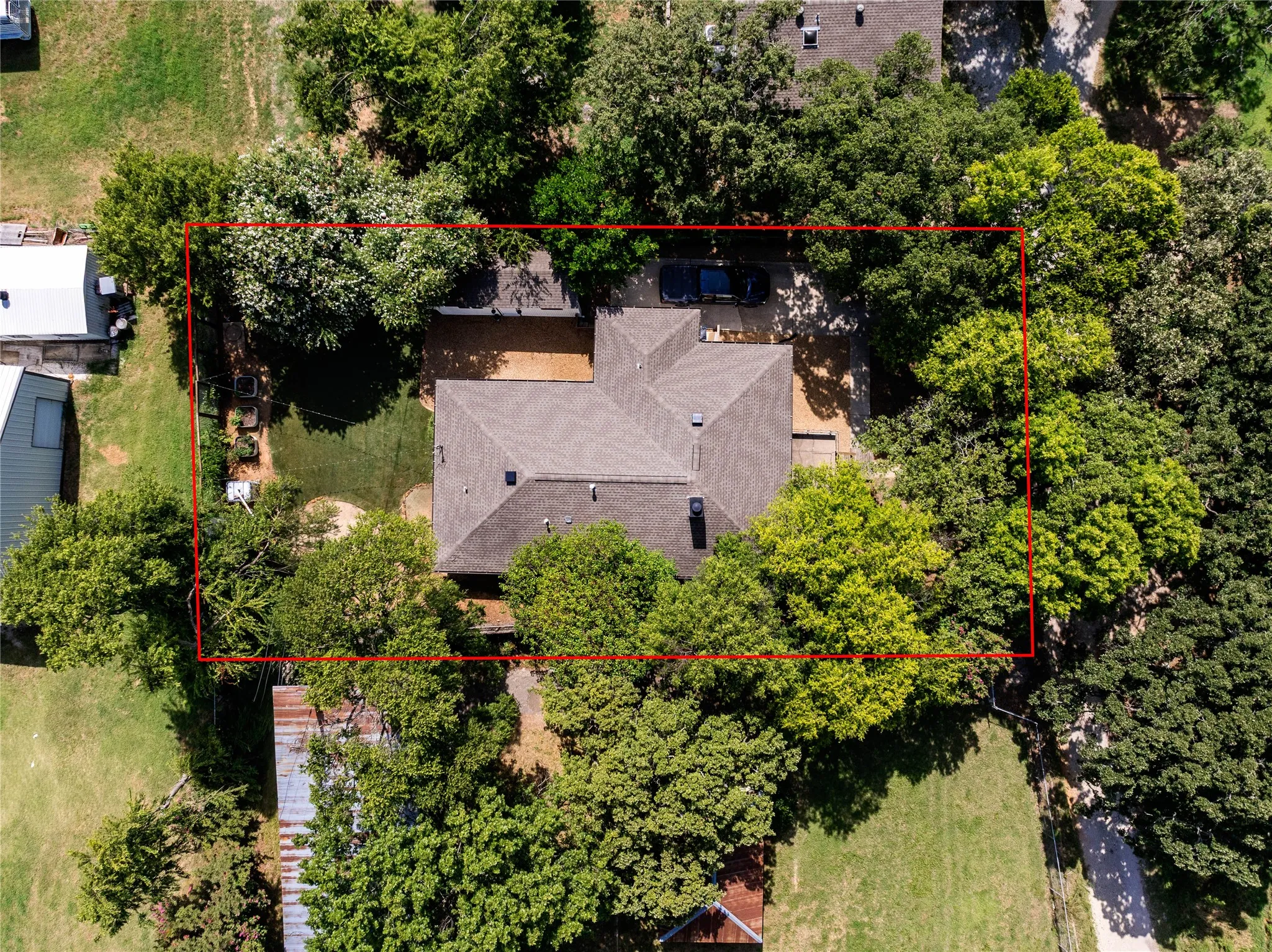 Aerial perspective showcasing a single-story residence with a gray shingle roof, surrounded by mature trees