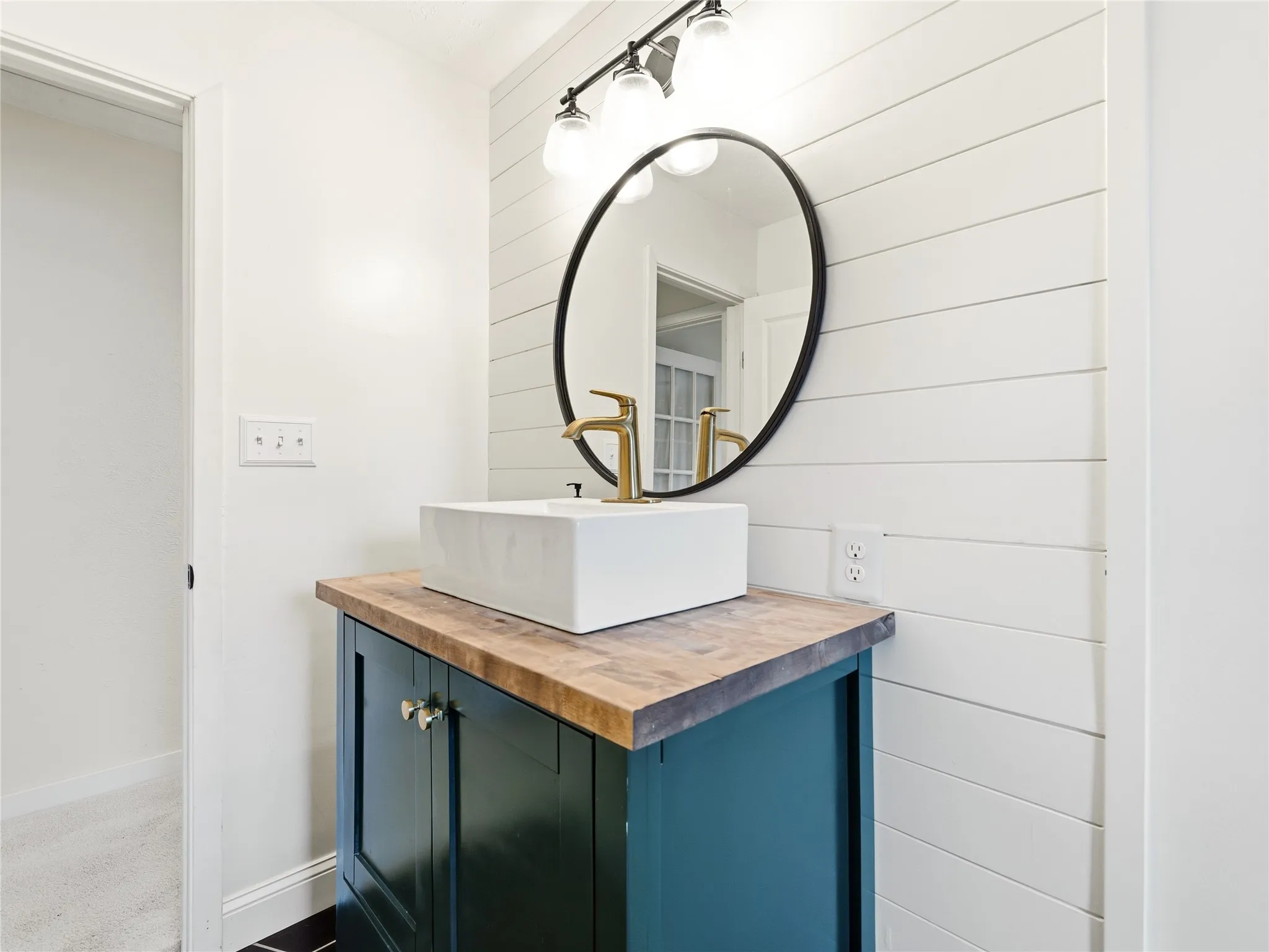 Vanity with a wood-finish countertop, white vessel sink, and brass faucet