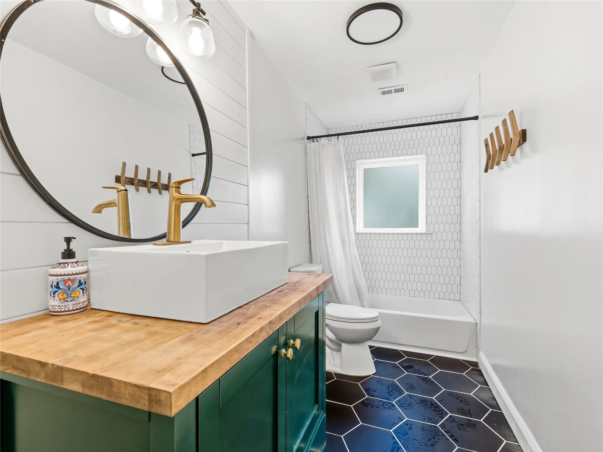 Bathroom featuring a dark green vanity with wood-finish countertop, rectangular vessel sink with gold-tone faucet, and a large round mirror