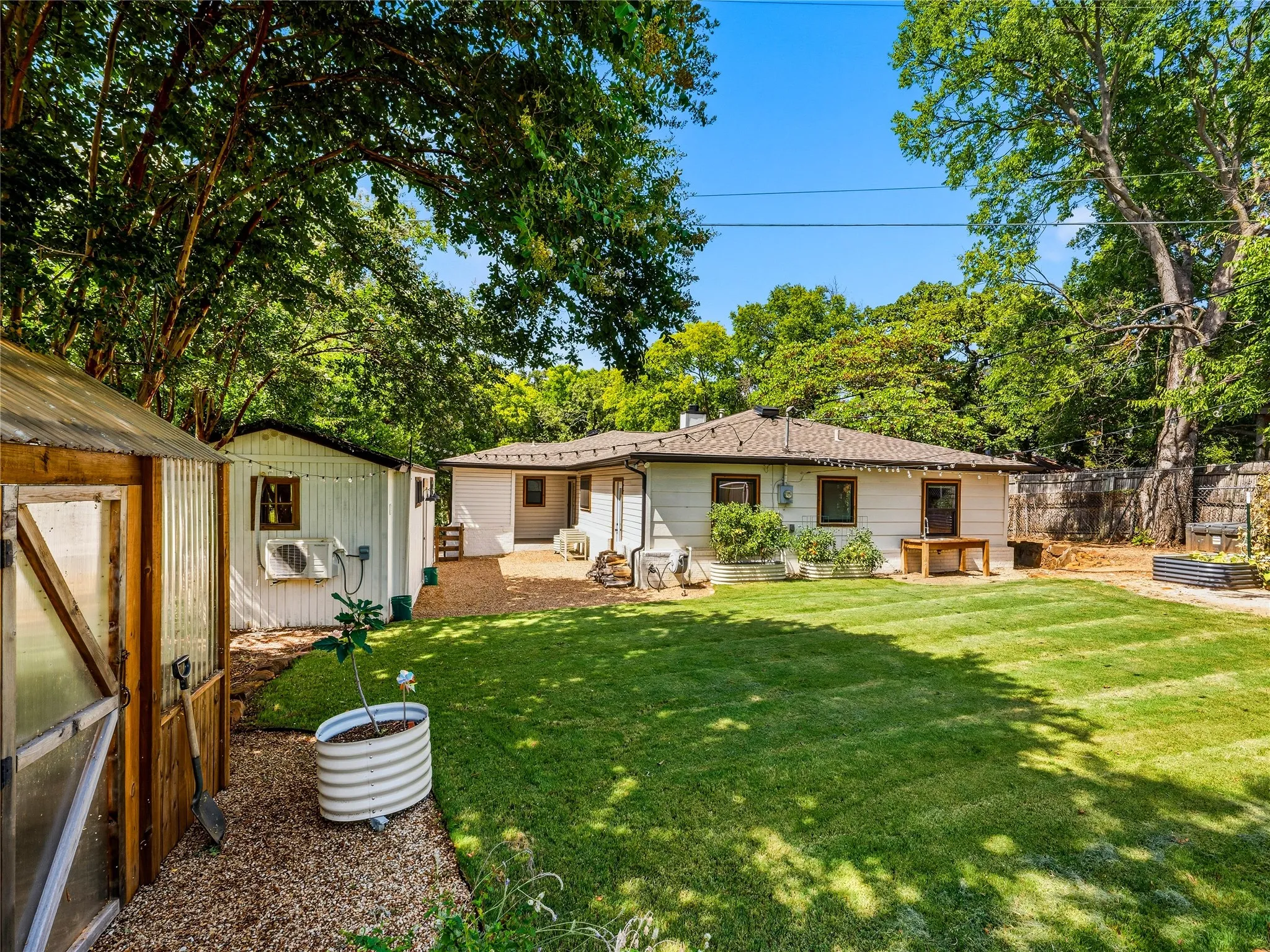 Expansive lawn area featuring a gravel pathway, mature trees, a detached storage shed, and a greenhouse structure