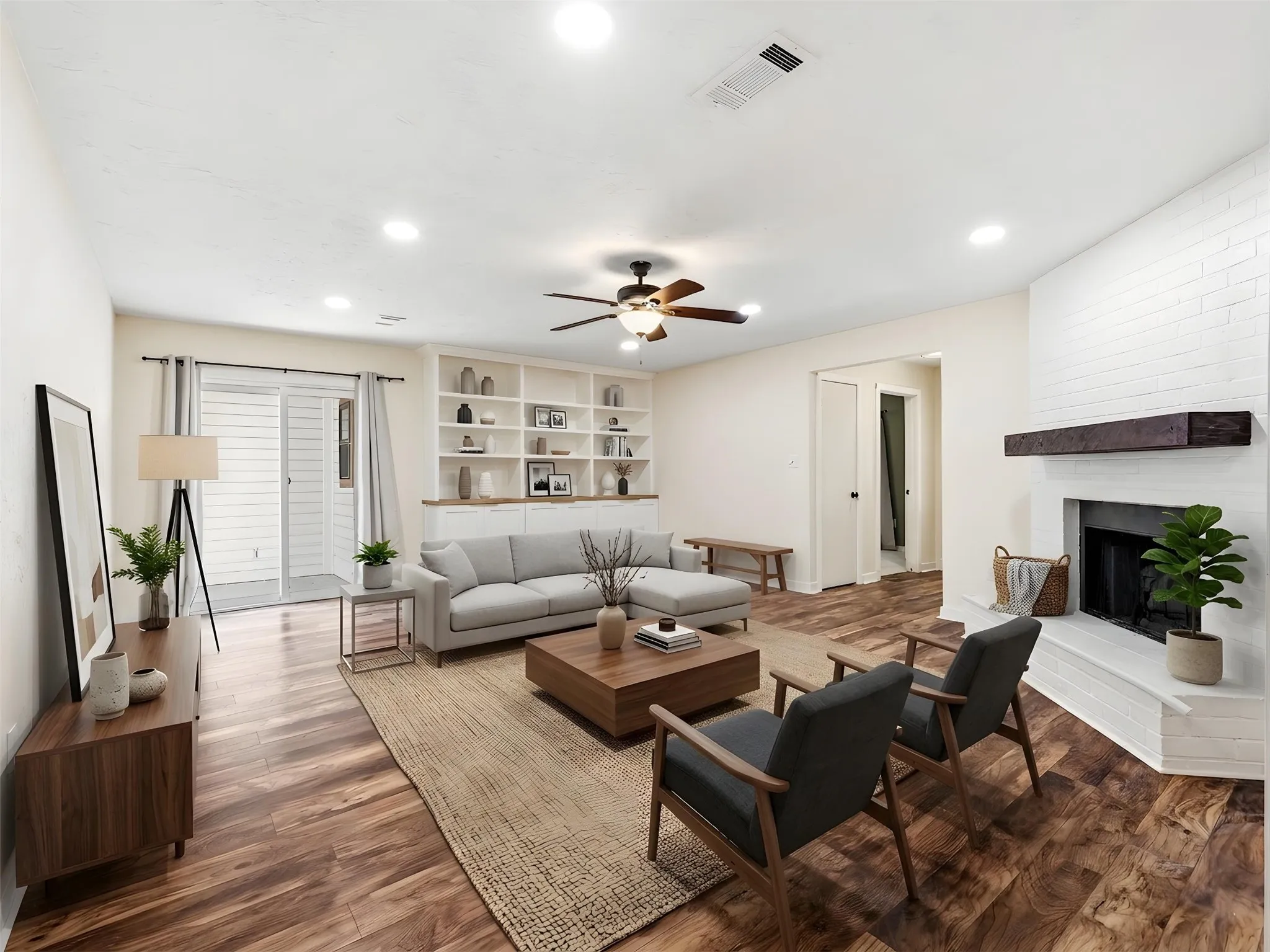 Spacious living area featuring wood-finish flooring, a white brick fireplace with a substantial wood mantel, built-in shelving, and recessed lighting
