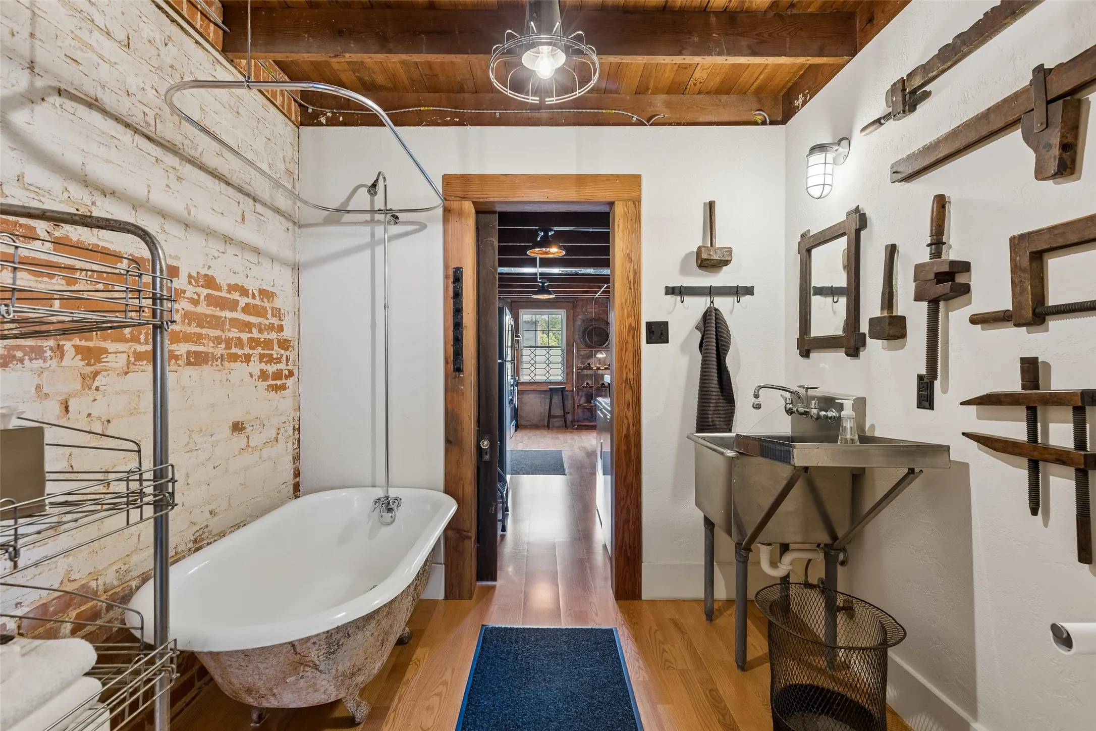 Bathroom featuring a clawfoot tub with shower attachment, exposed brick wall, wood-finish flooring, wood plank ceiling, and a double basin utility sink