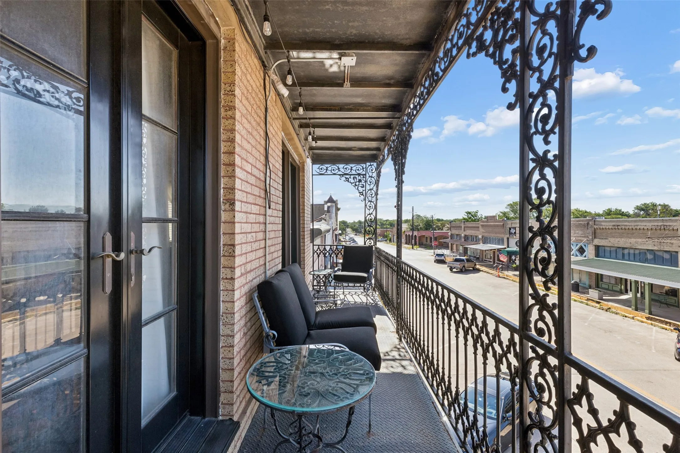 Expansive balcony featuring ornate ironwork railings, brick exterior, and multiple glass-paneled doors providing access to interior spaces