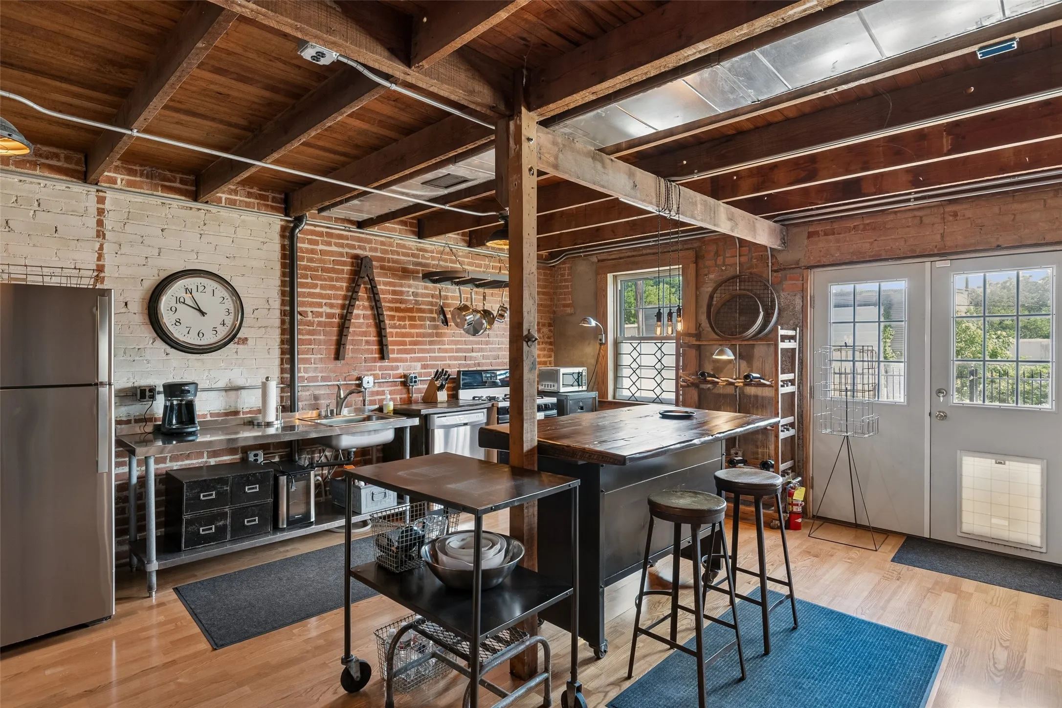 Exposed brick walls, wood-finish flooring, and exposed wood beam ceilings define this kitchen space