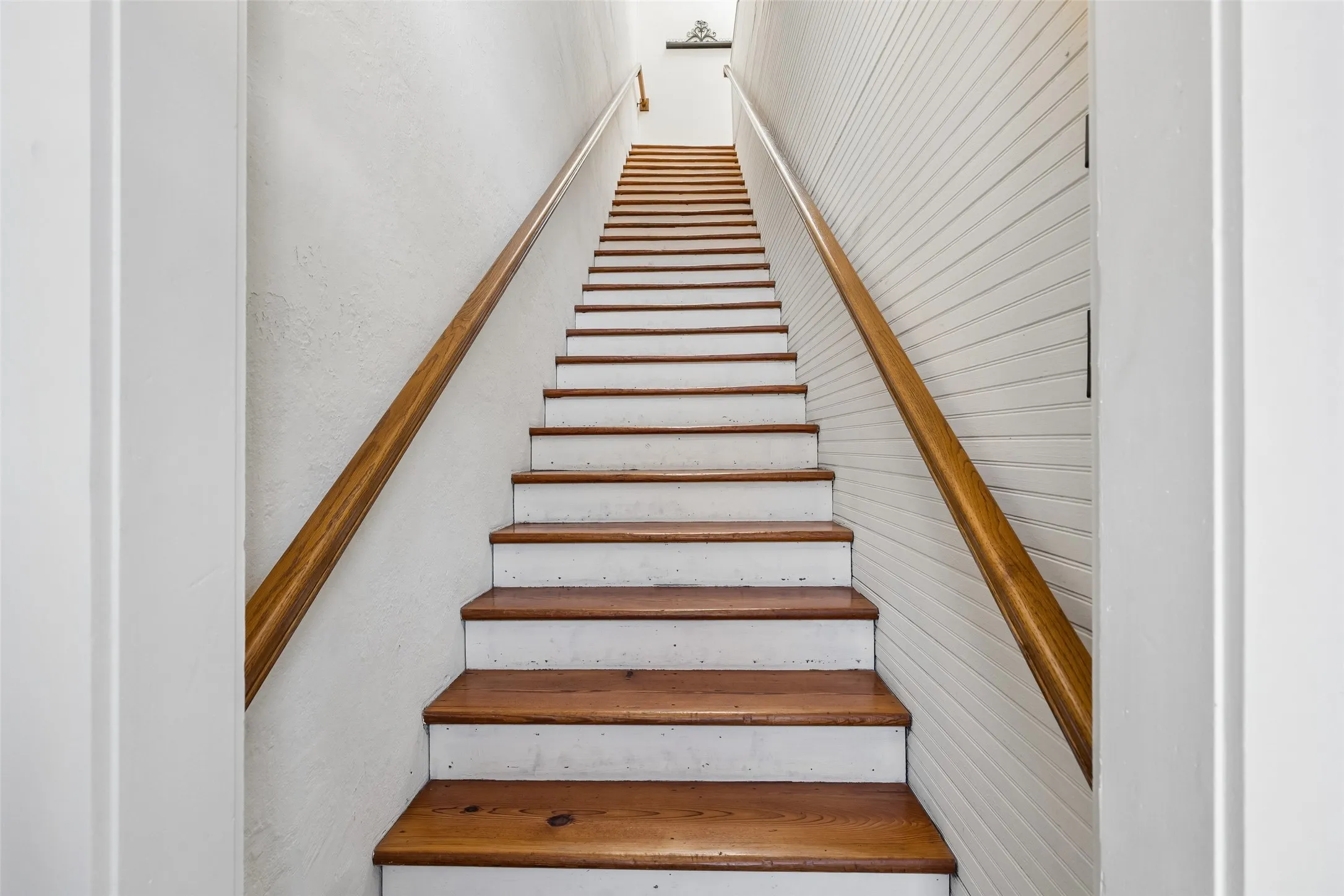 Staircase featuring wood-finish treads and handrails, white risers, and textured wall finishes