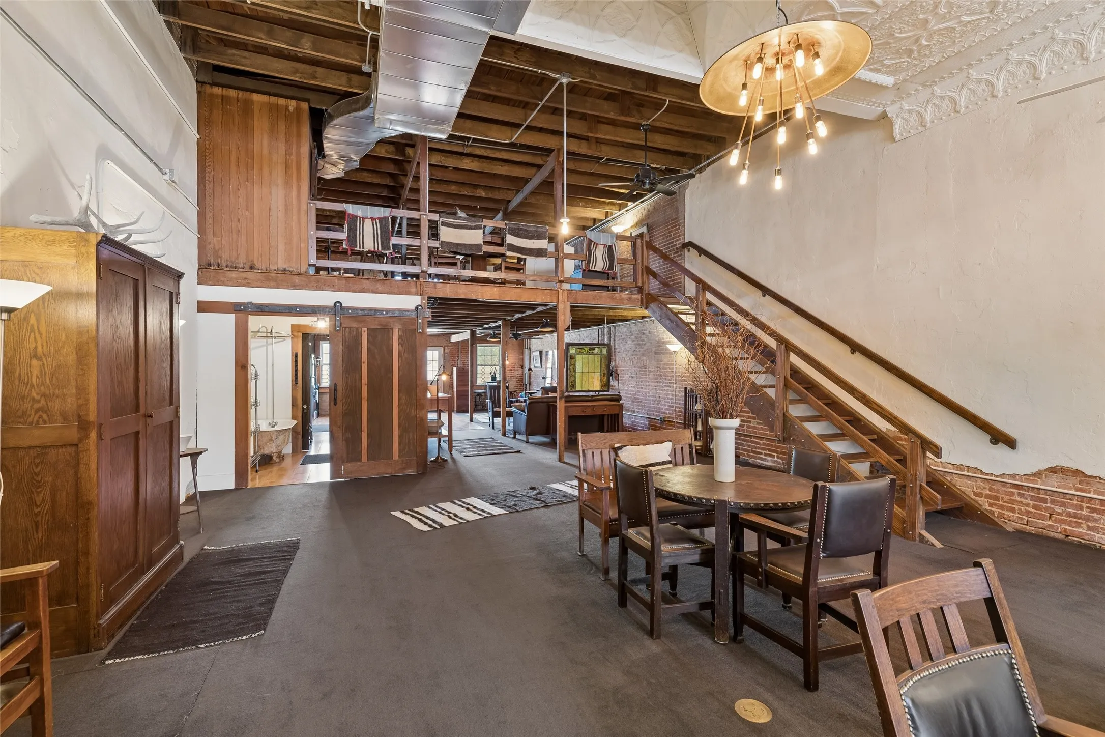 Open-concept living space featuring high ceilings with exposed wood beams, a prominent wooden staircase, and industrial-style ductwork