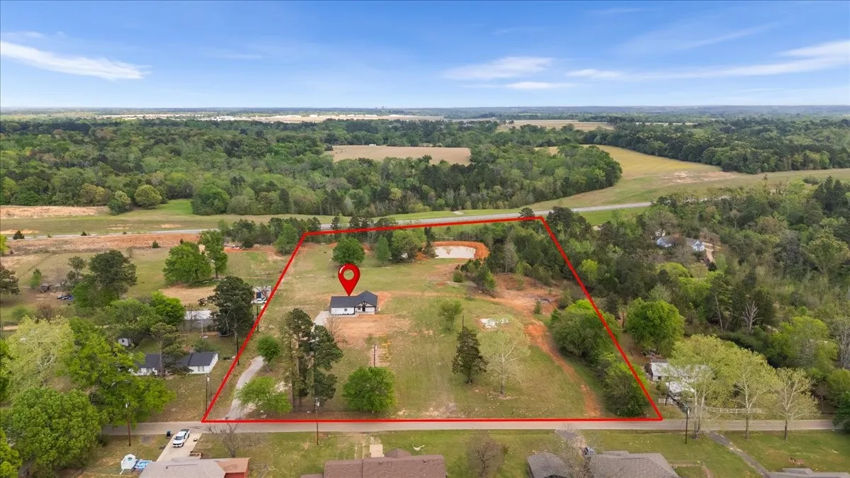 Aerial view of a property featuring a single-story residence, a private pond, and extensive wooded surroundings