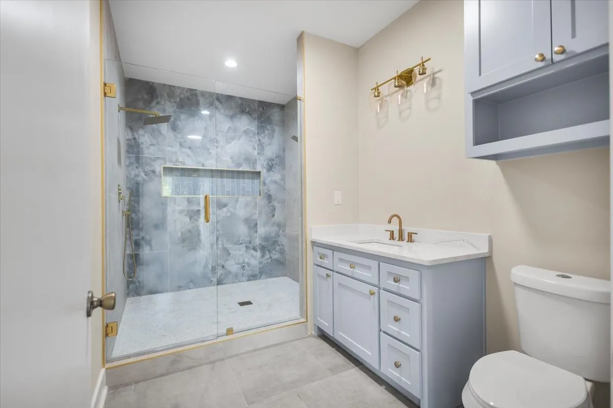Shower with glass enclosure, rain shower head, and built-in niche, alongside a vanity with a white countertop and blue cabinetry