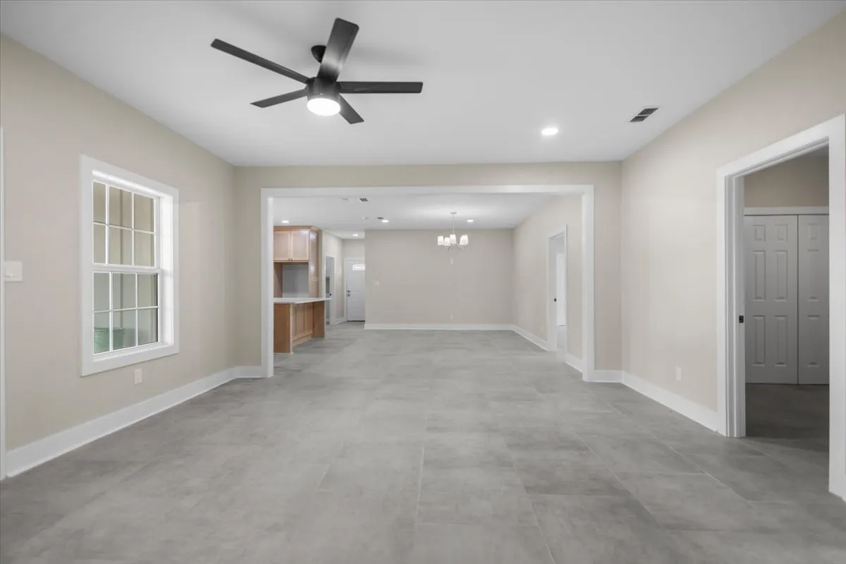 Spacious living area featuring large format grey tile flooring, a modern ceiling fan, recessed lighting, and a window with white trim