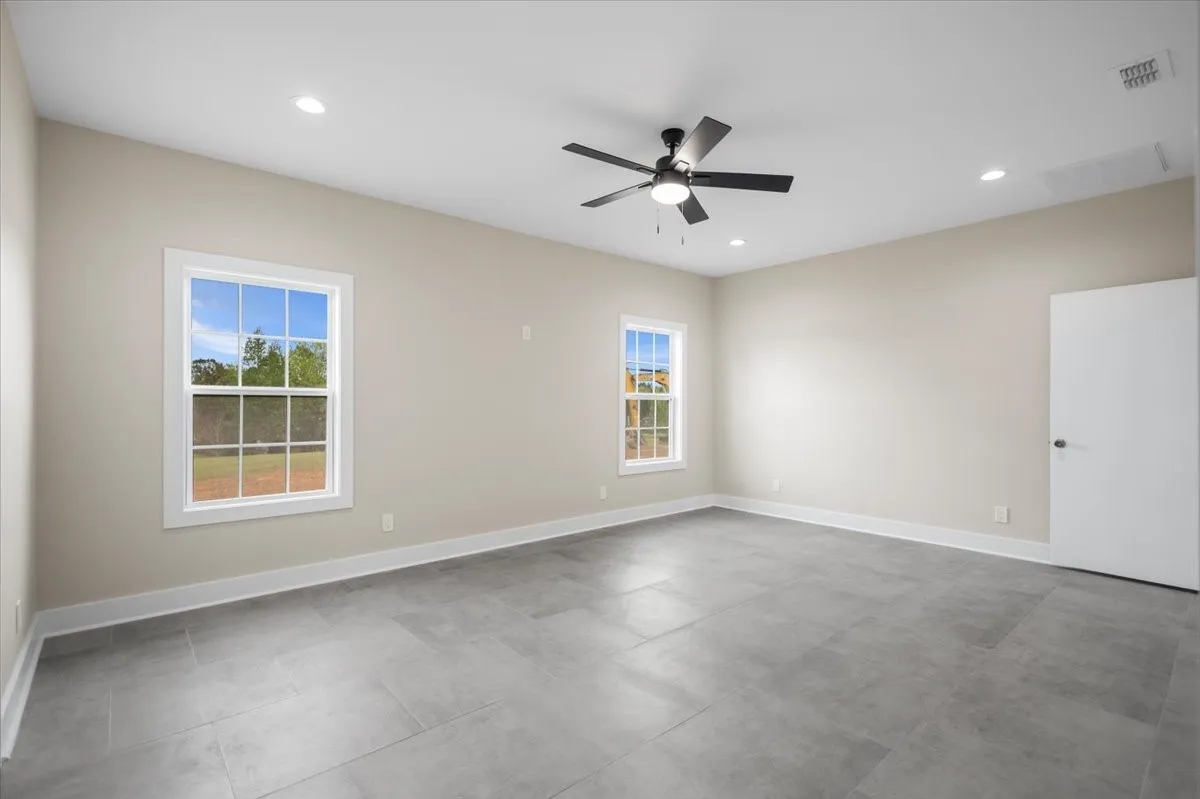 Spacious room featuring gray tile flooring, two double-hung windows with white trim, recessed lighting, and a black ceiling fan with integrated light
