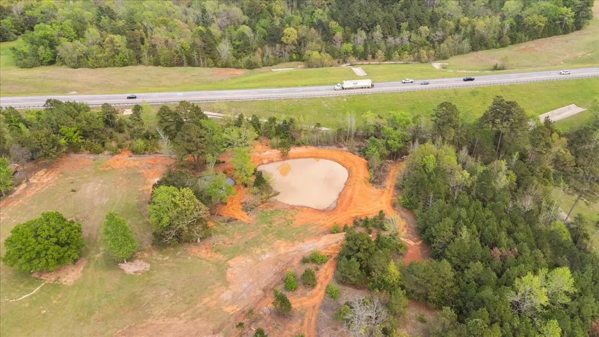 Expansive land parcel featuring a natural pond, mature tree coverage, and a paved highway frontage