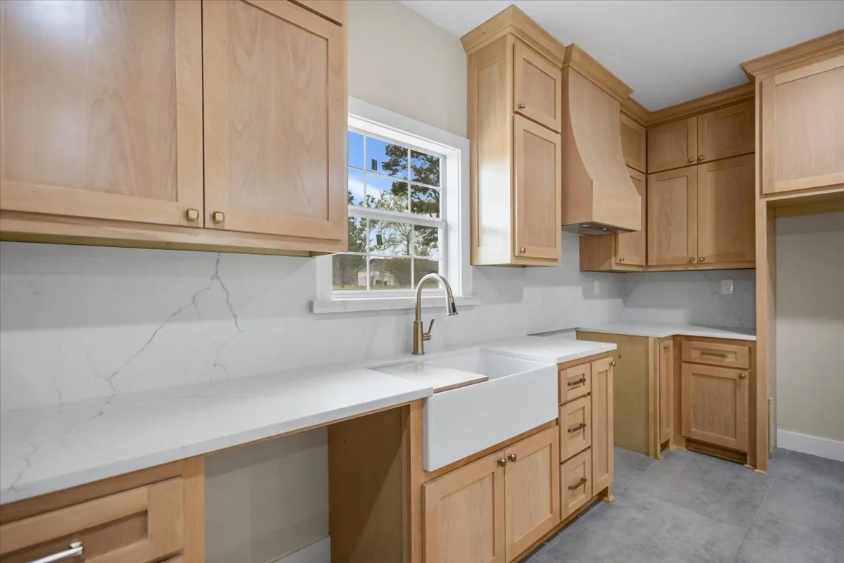 Light-toned cabinetry with brass hardware, a farmhouse sink with a gooseneck faucet, a light countertop with integrated backsplash, and light grey flooring