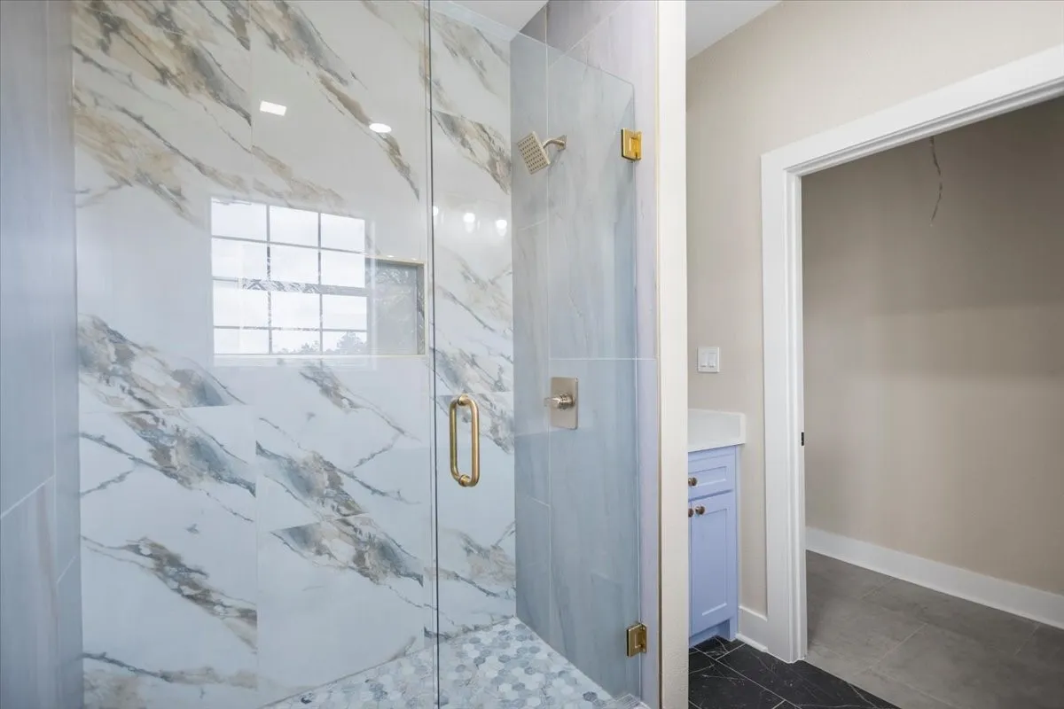 Glass-enclosed shower featuring large format marble-look tile walls, a hexagonal mosaic tile floor, and a built-in shower niche