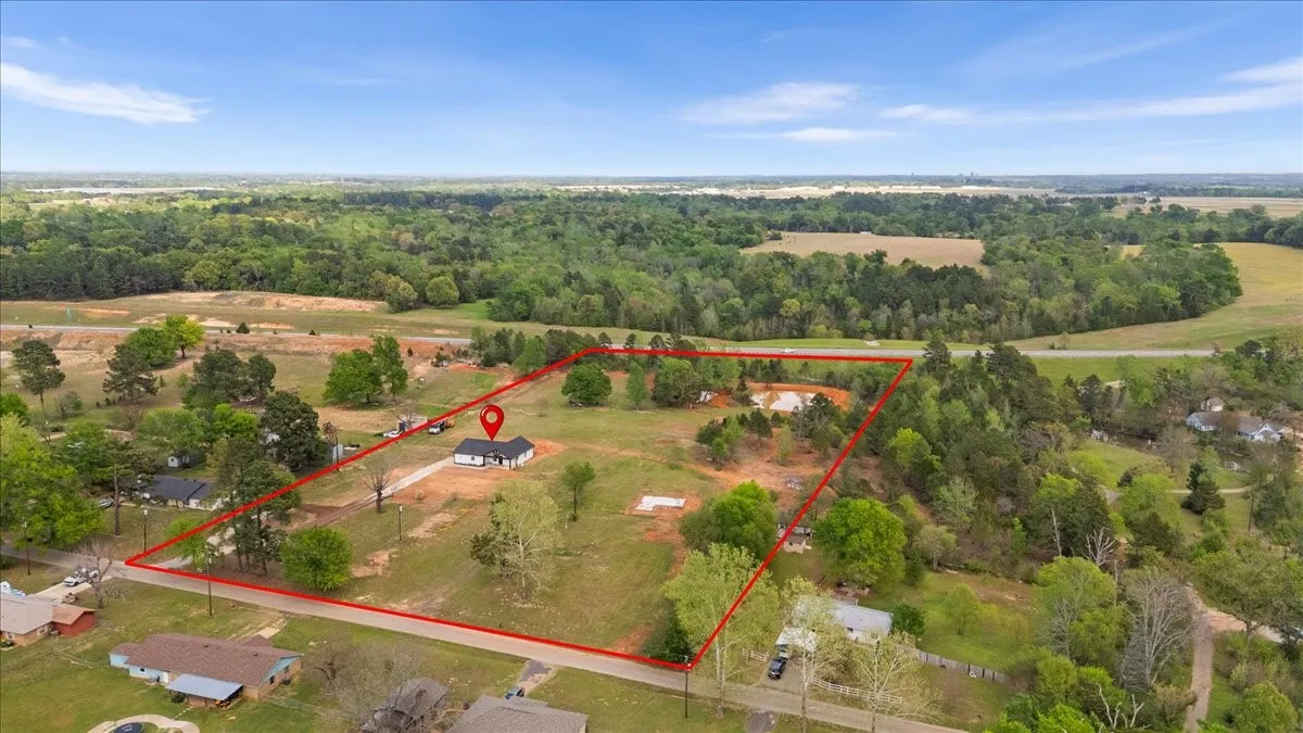 Aerial perspective showcasing a single-story residence with a dark roof situated on a expansive, tree-dotted parcel