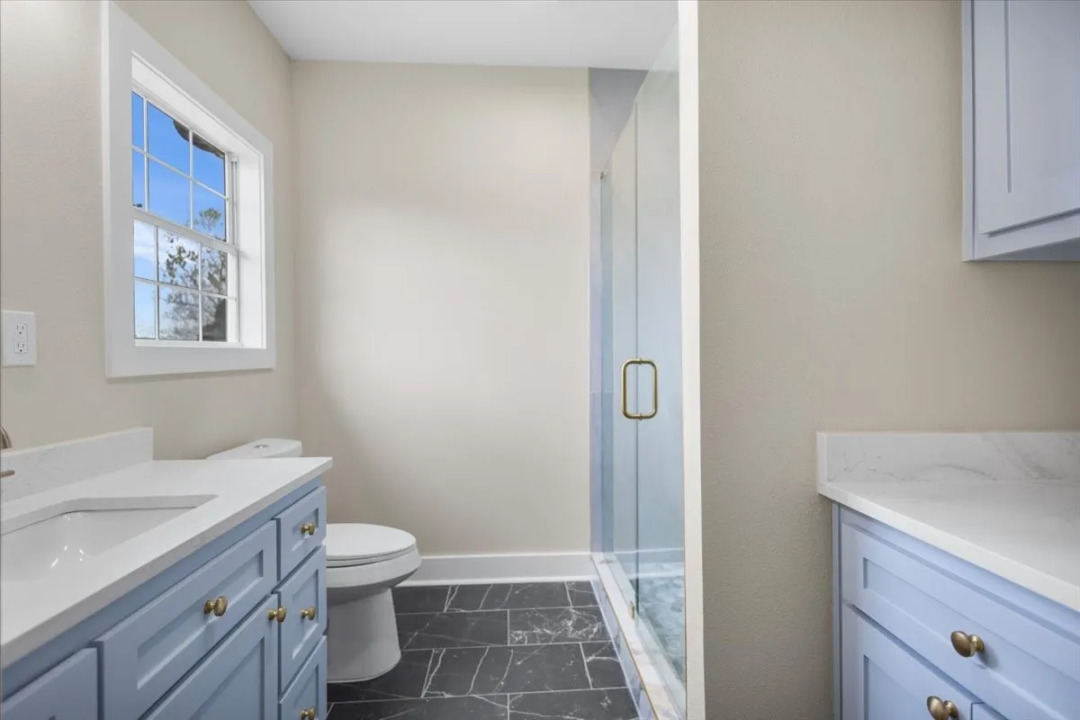 Bathroom with a walk-in glass shower, double-hung window, and slate-style tile flooring