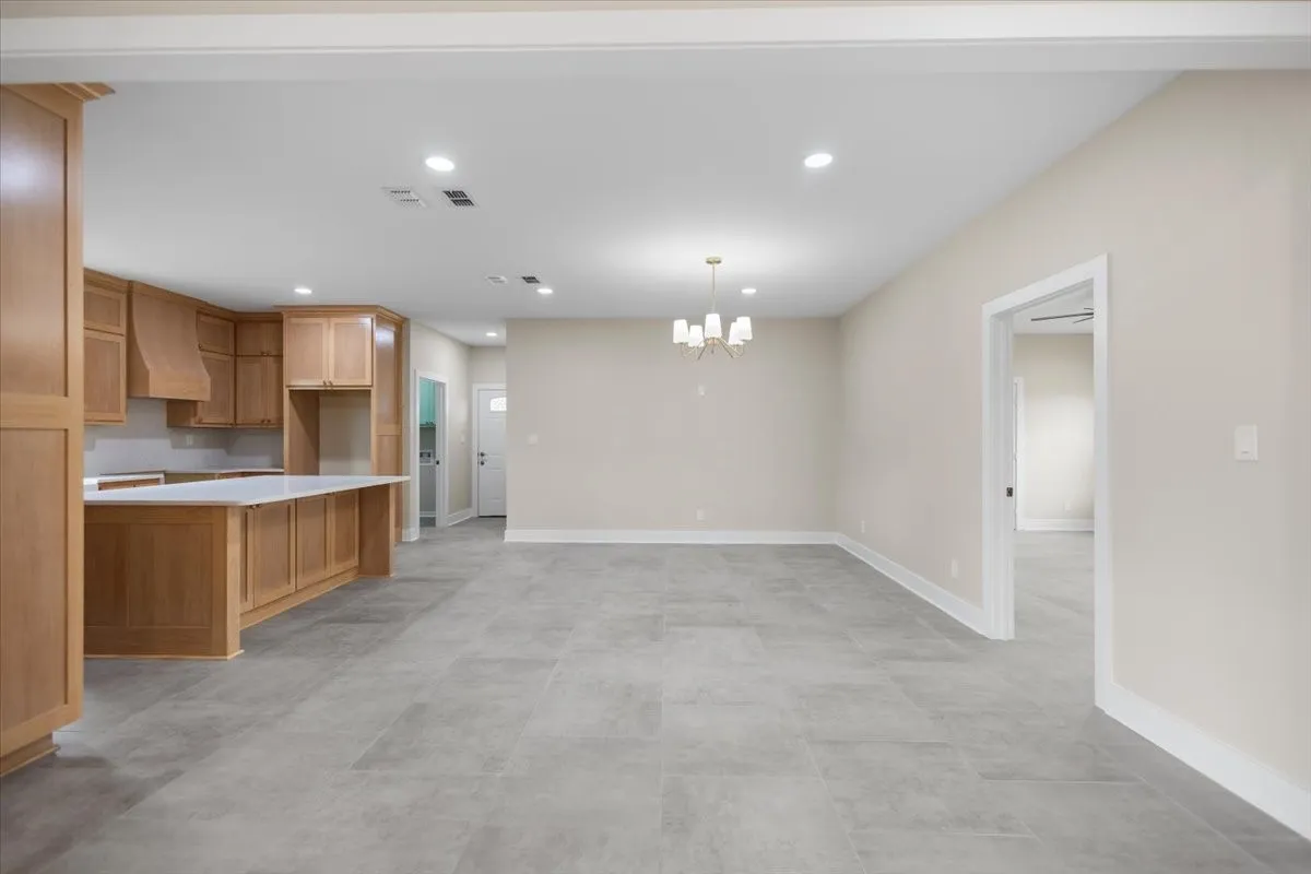 Open-concept living space featuring a kitchen with light wood cabinetry and white countertops, grey tile flooring, recessed lighting, and a contemporary chandelier