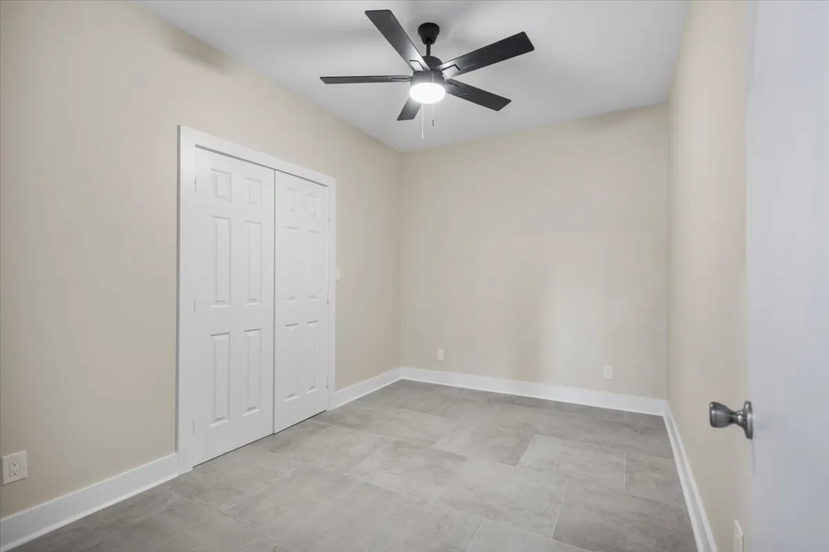Neutral-toned room featuring light gray tile flooring, white trim, and a ceiling fan with black blades
