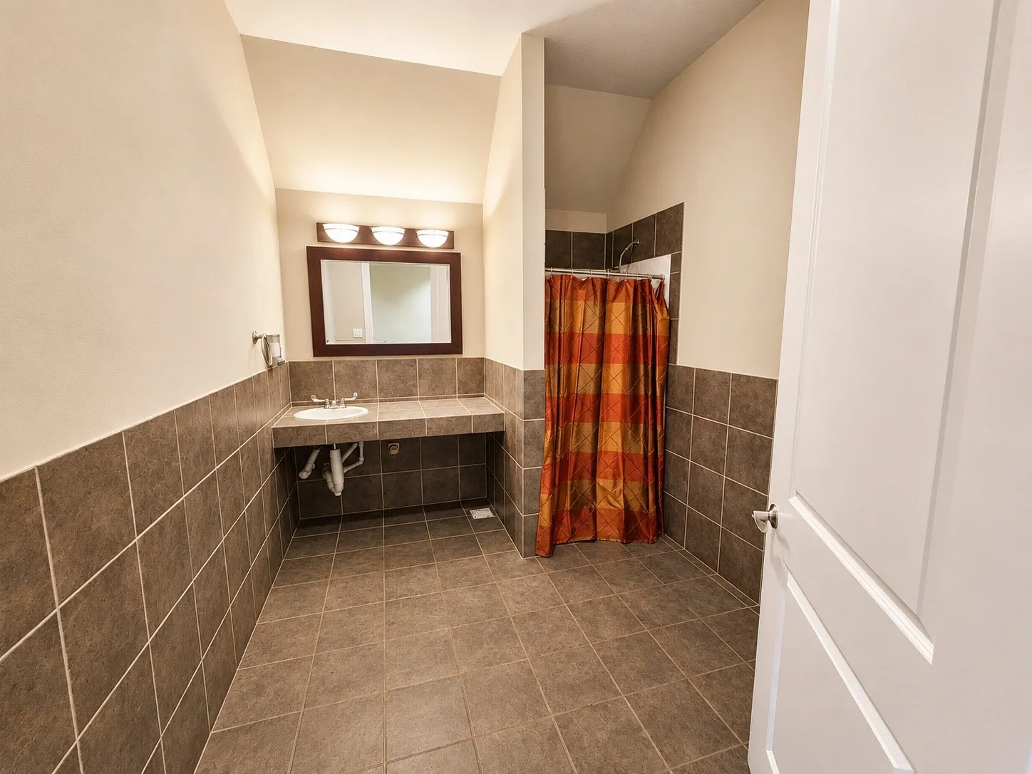 Spacious bathroom featuring large format floor tiles, coordinating wainscoting, and a single vanity with an integrated sink