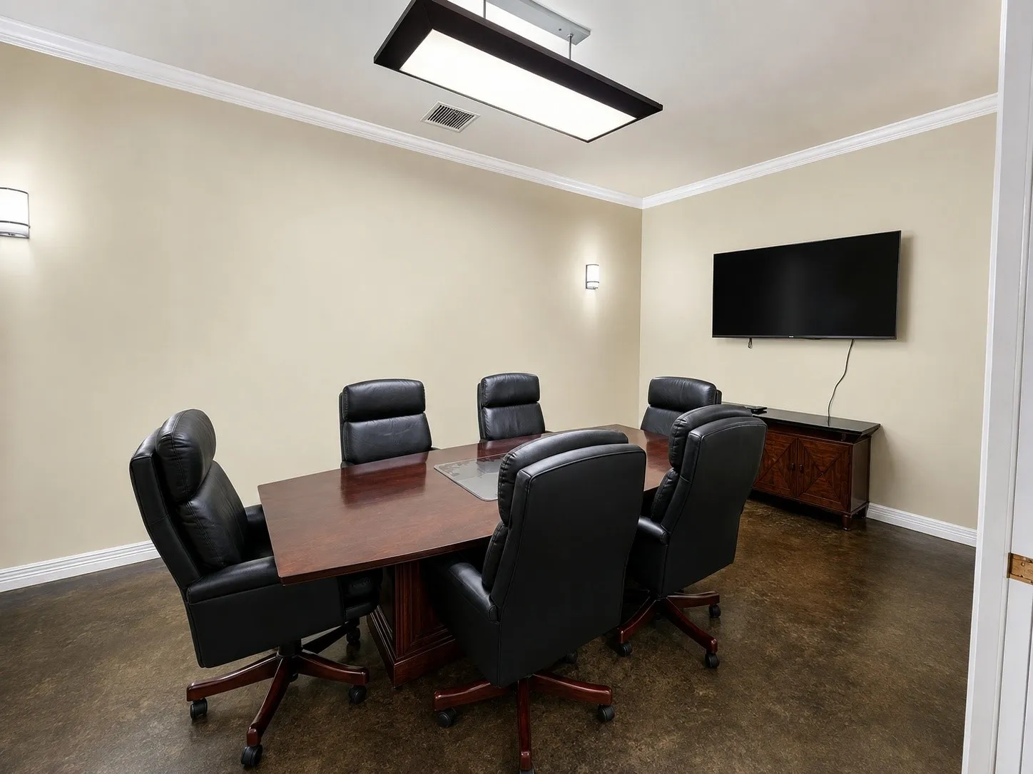 Conference room featuring a dark wood-finish table with six chairs, a wall-mounted display, and recessed wall sconces