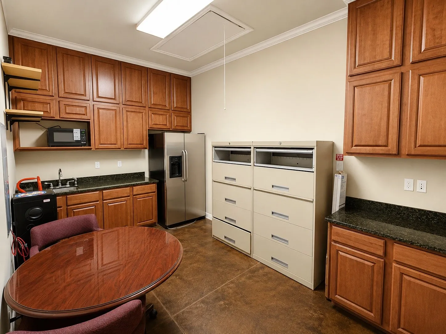 Spacious utility area featuring extensive wood cabinetry, dark granite-look countertops, and durable concrete-finish flooring