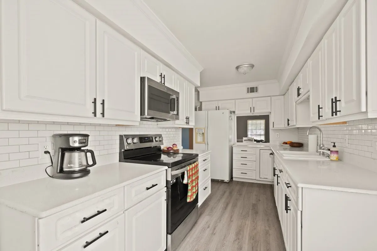 Galley kitchen featuring white cabinetry with black hardware, white countertops, a subway tile backsplash, stainless steel microwave, and wood-finish flooring