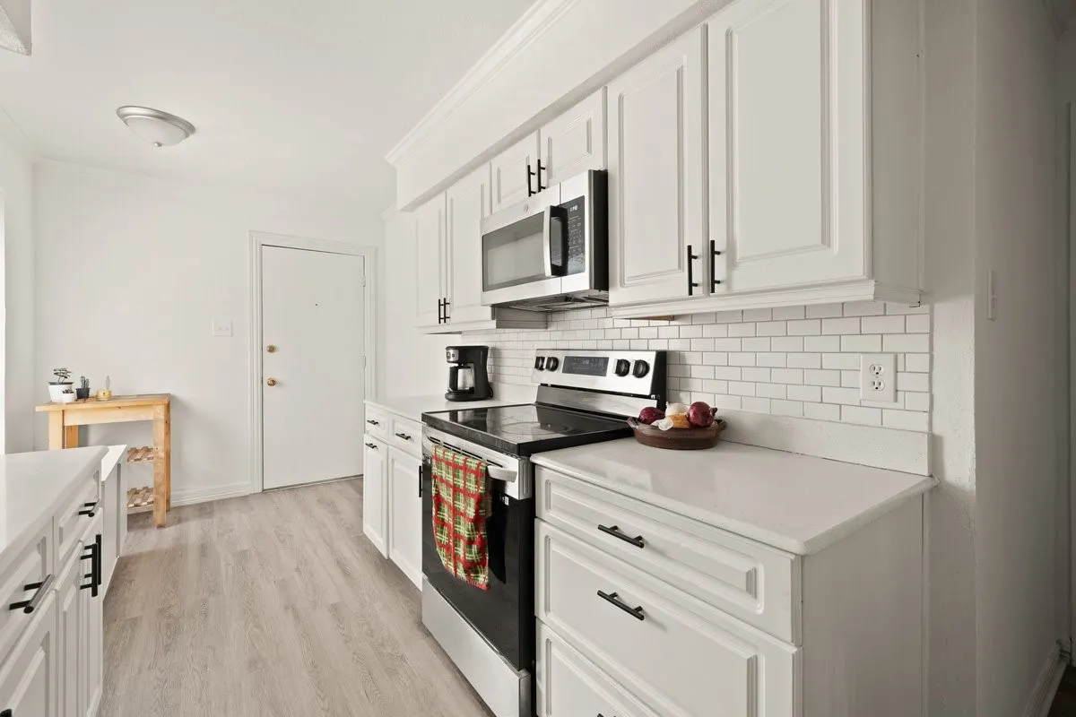 Bright kitchen featuring white cabinetry, stainless steel appliances, a subway tile backsplash, light wood-finish flooring, and solid surface countertops