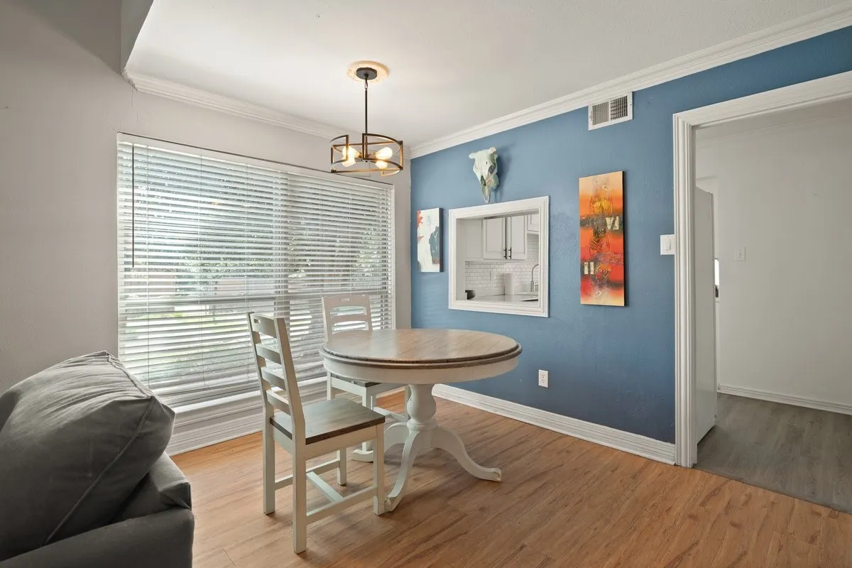 Dining area featuring wood-finish flooring, a contemporary ceiling light fixture, a pass-through window with white trim, a large window with blinds, and crown molding